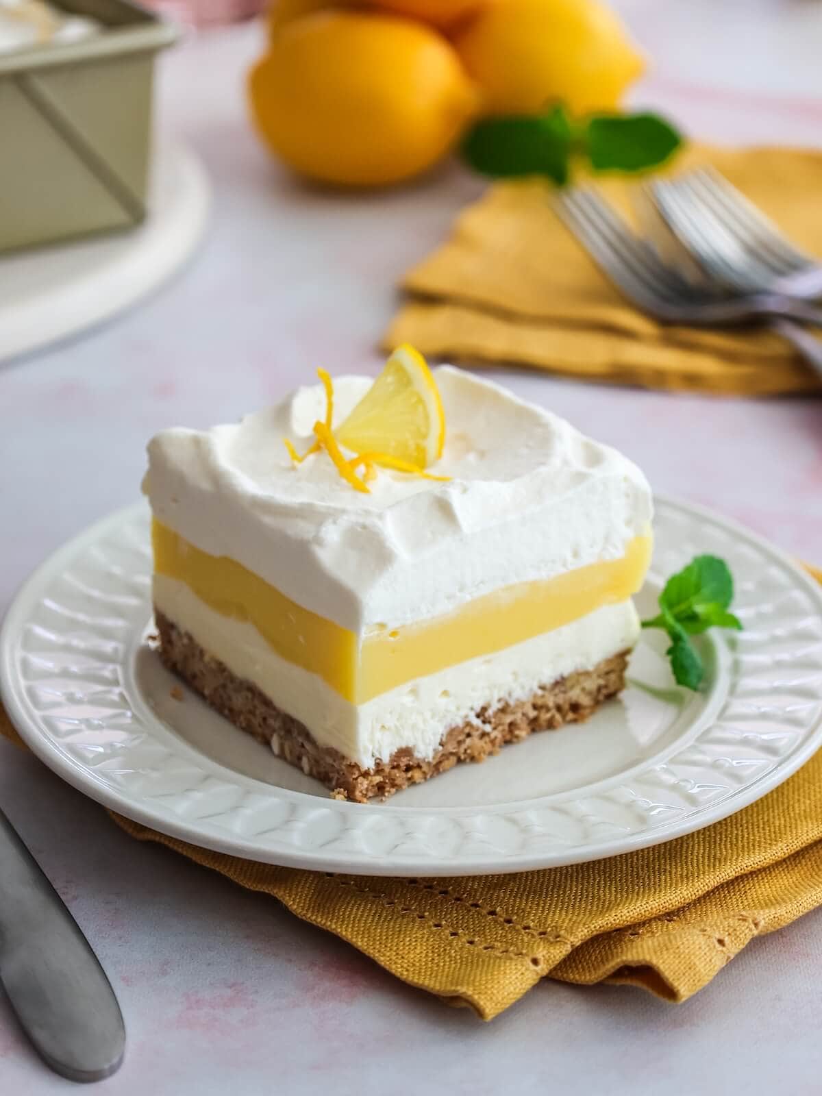 lemon lush dessert on a plate with a mint sprig. Lemons in the back.