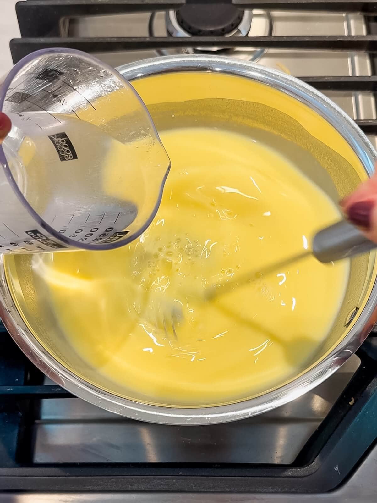 adding hot water to the lemon curd on the stove.