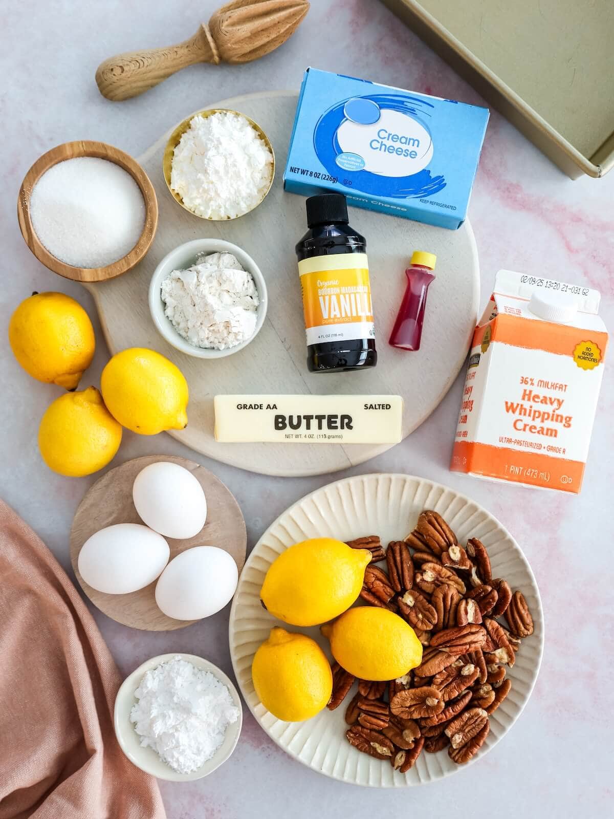Ingredients for lemon lush arranged on a variety of surfaces and cutting boards, including lemons, pecans, eggs, cream, cream cheese, flour, sugar and vanilla.