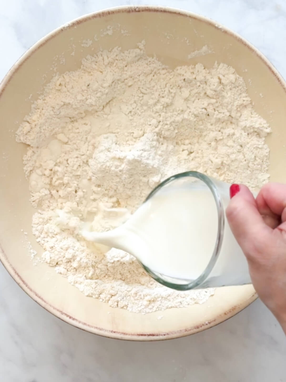 Adding milk to biscuit ingredients in a large bowl.