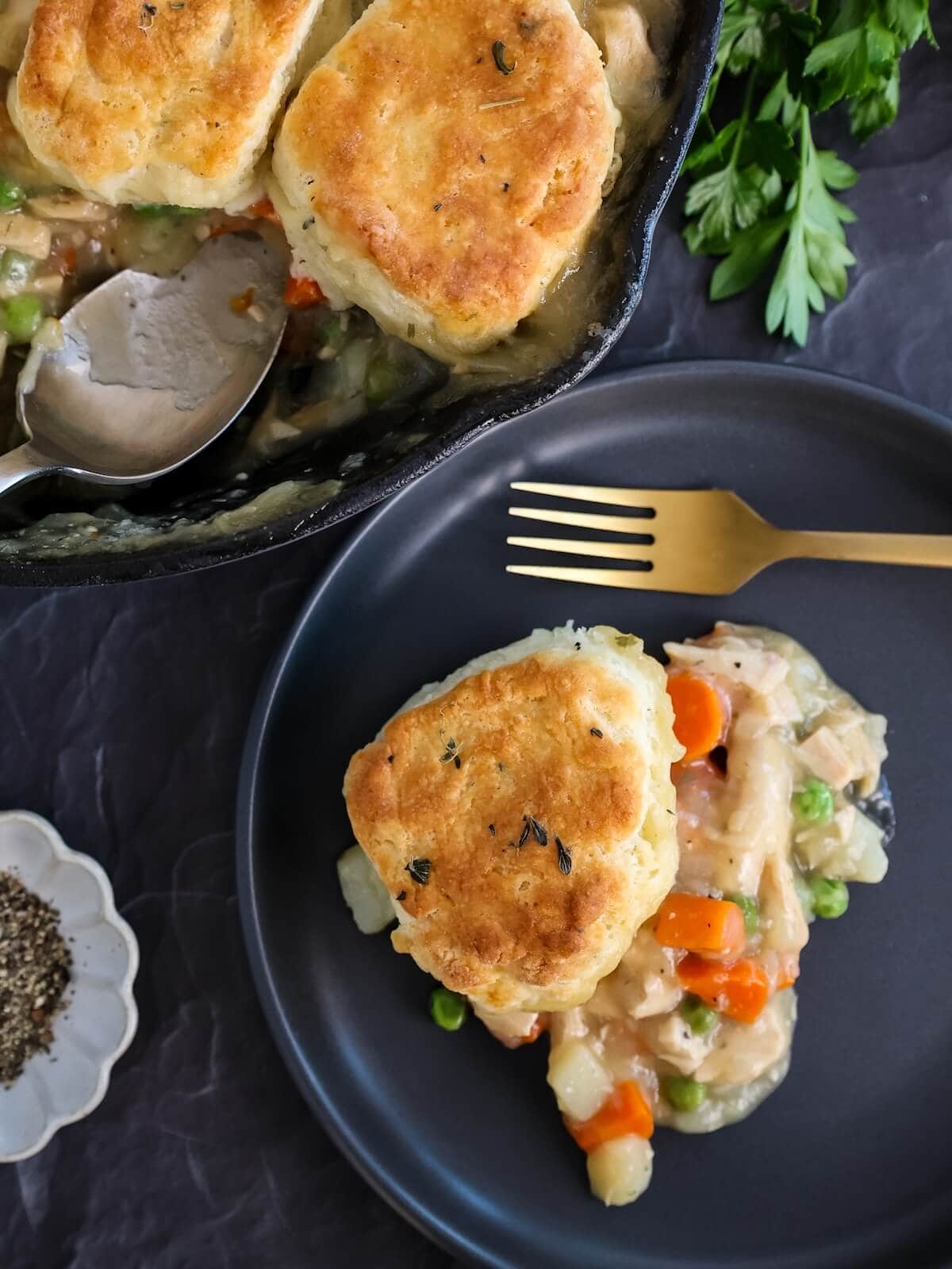 A serving of turkey pot pie with biscuit topping on a dark black plate.