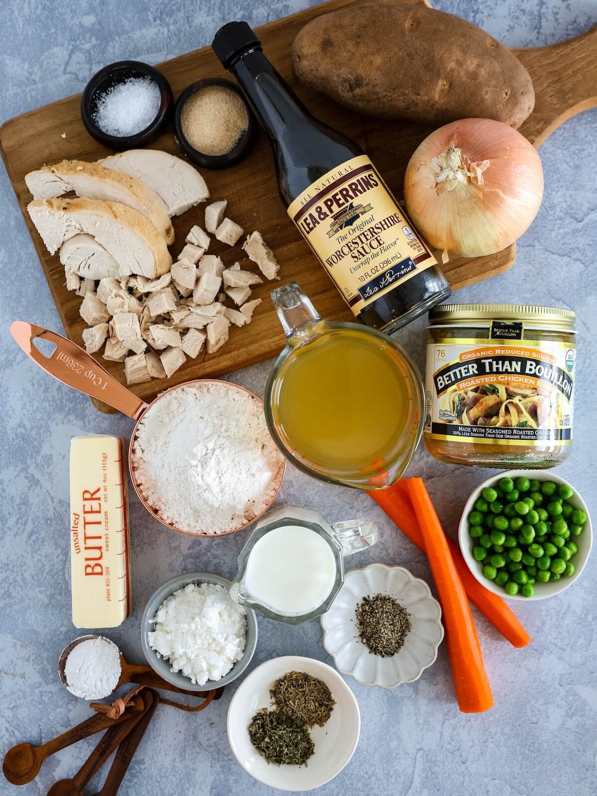 Ingredients for turkey pie with biscuits on a cutting board including broth, turkey, seasonings, potato, peas, carrots, and butter.