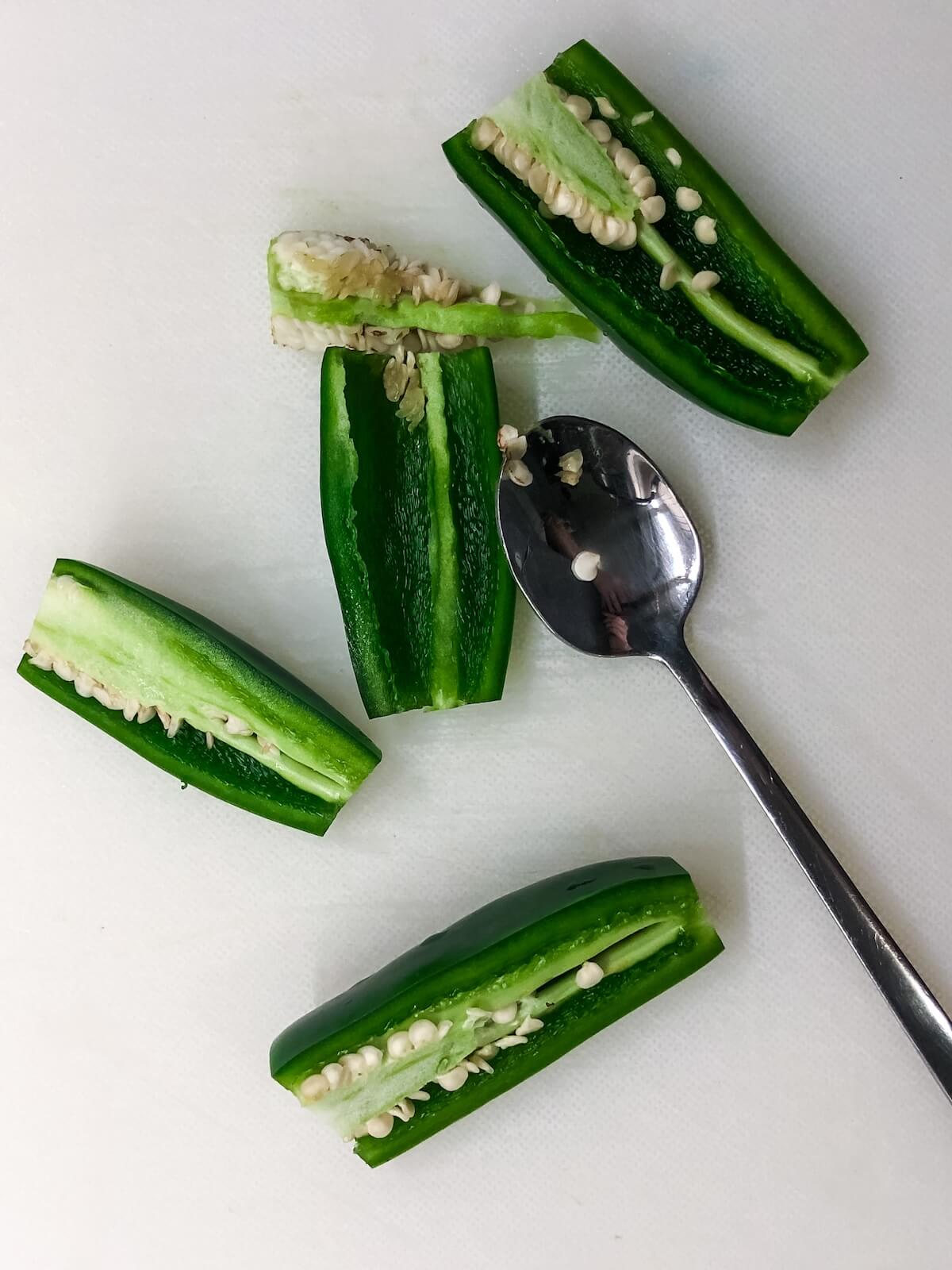 Use a spoon to scrape the seeds and pith from the inside of a jalapeno.