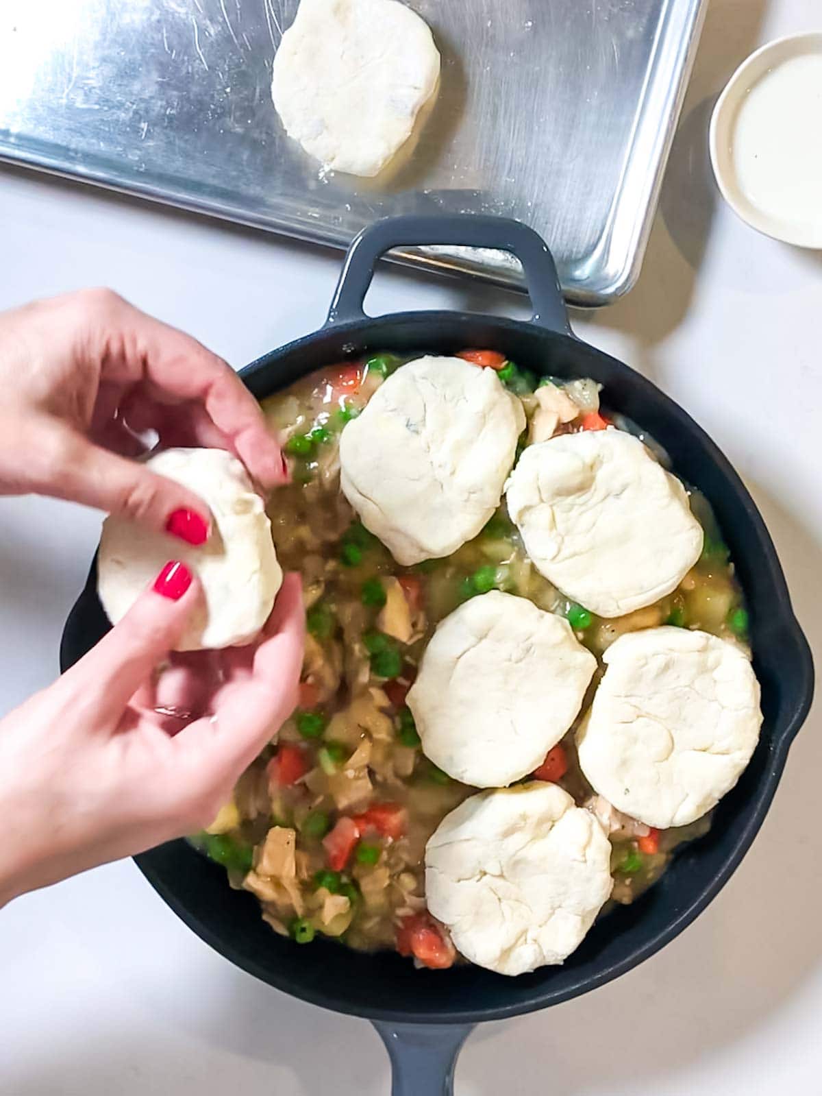 adding biscuits to turkey pot pie in a cast iron skillet.