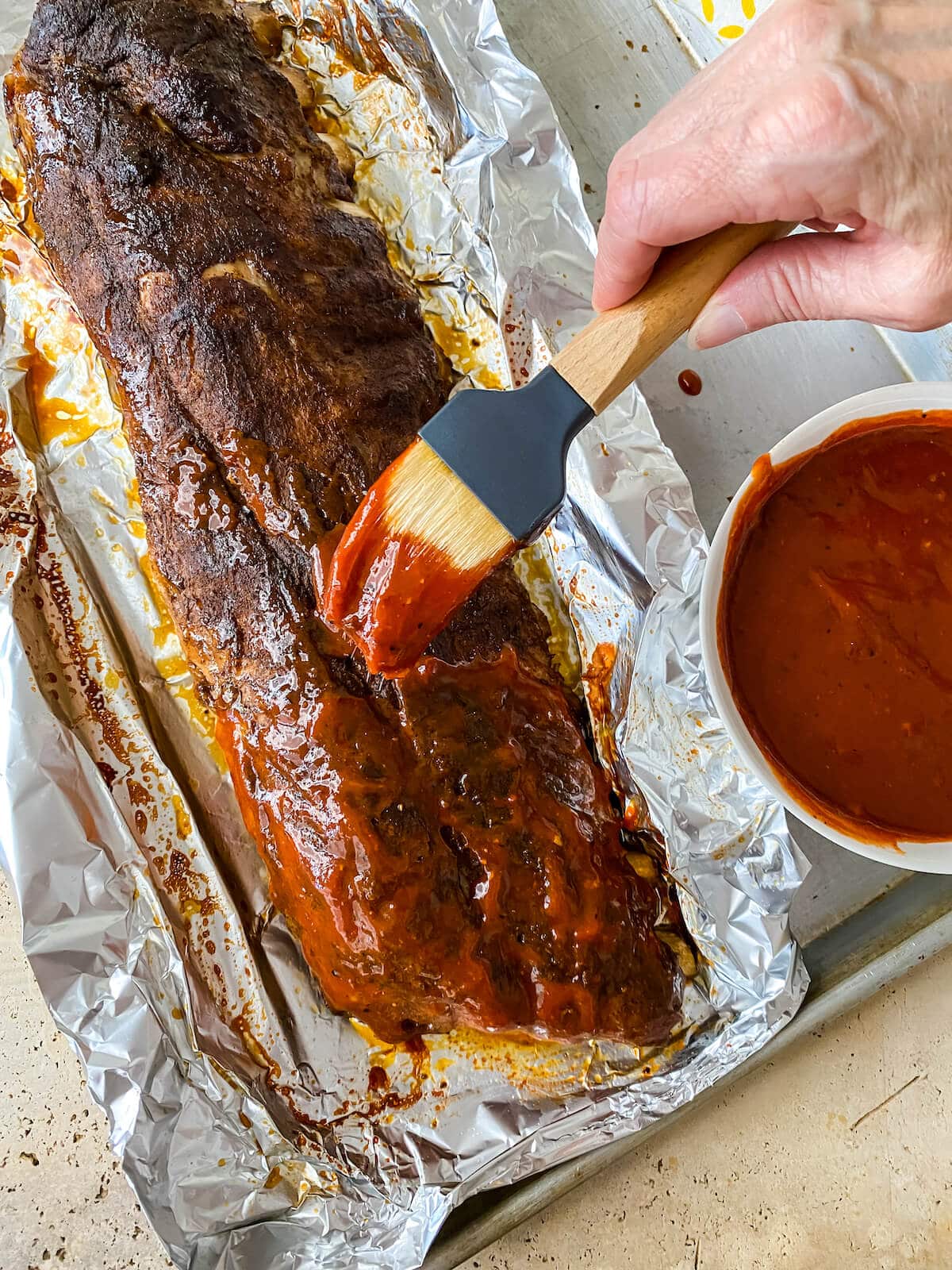 Brushing BBQ sauce on ribs cooked in the oven.