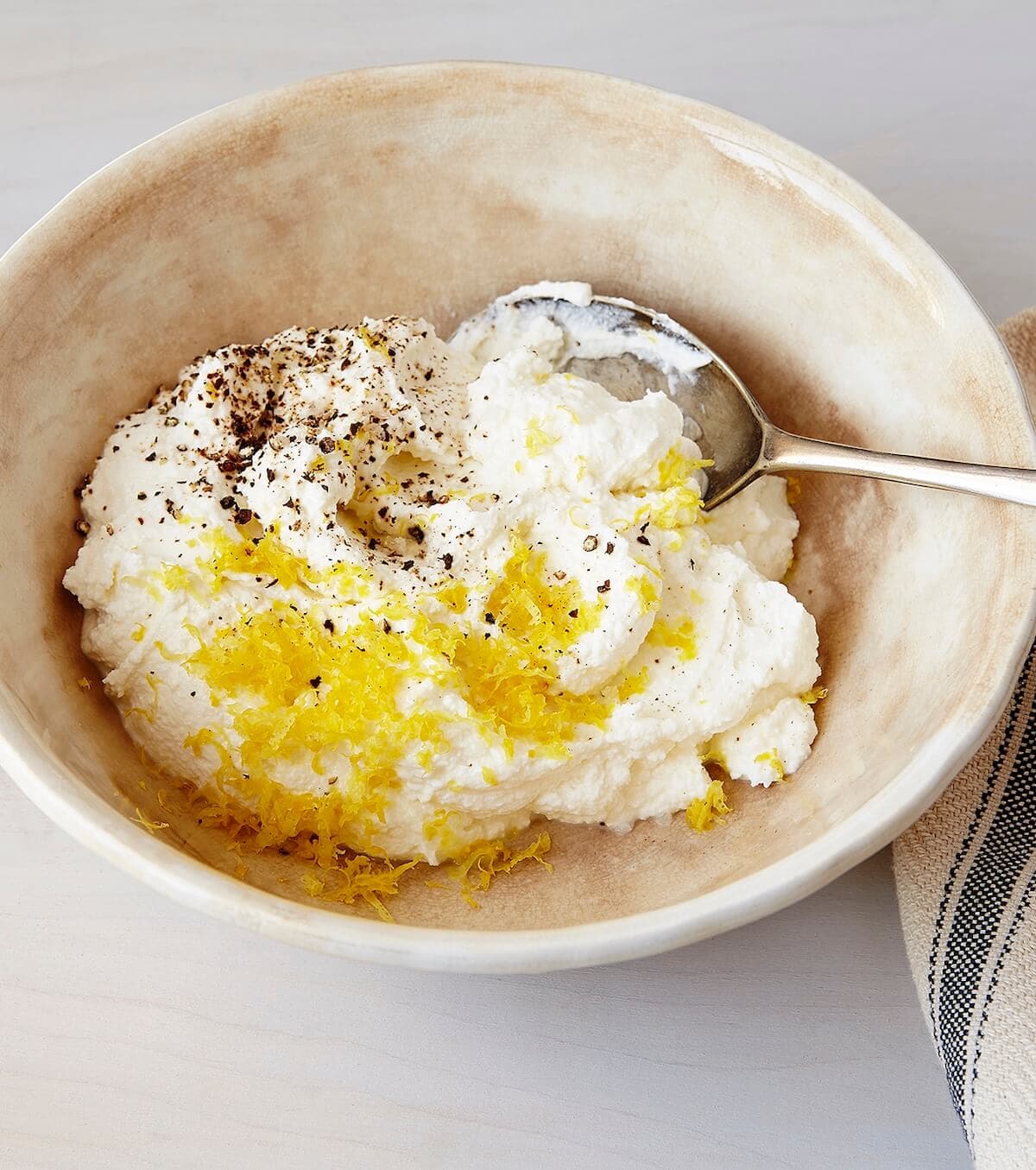Lemon ricotta being mixed in a bowl on a white background.