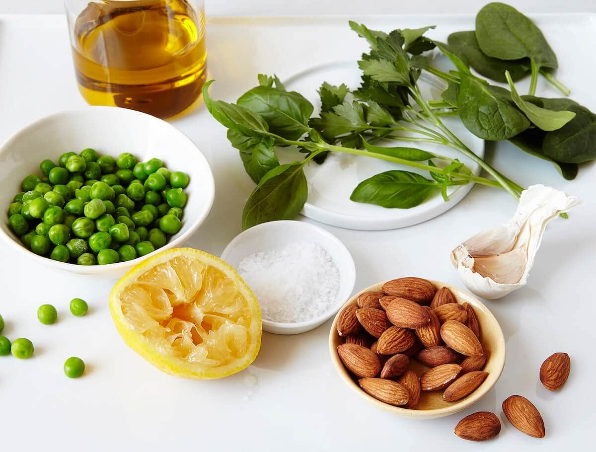 ingredients for winter pesto including almonds, lemon, garlic, salt, peas, and herbs.