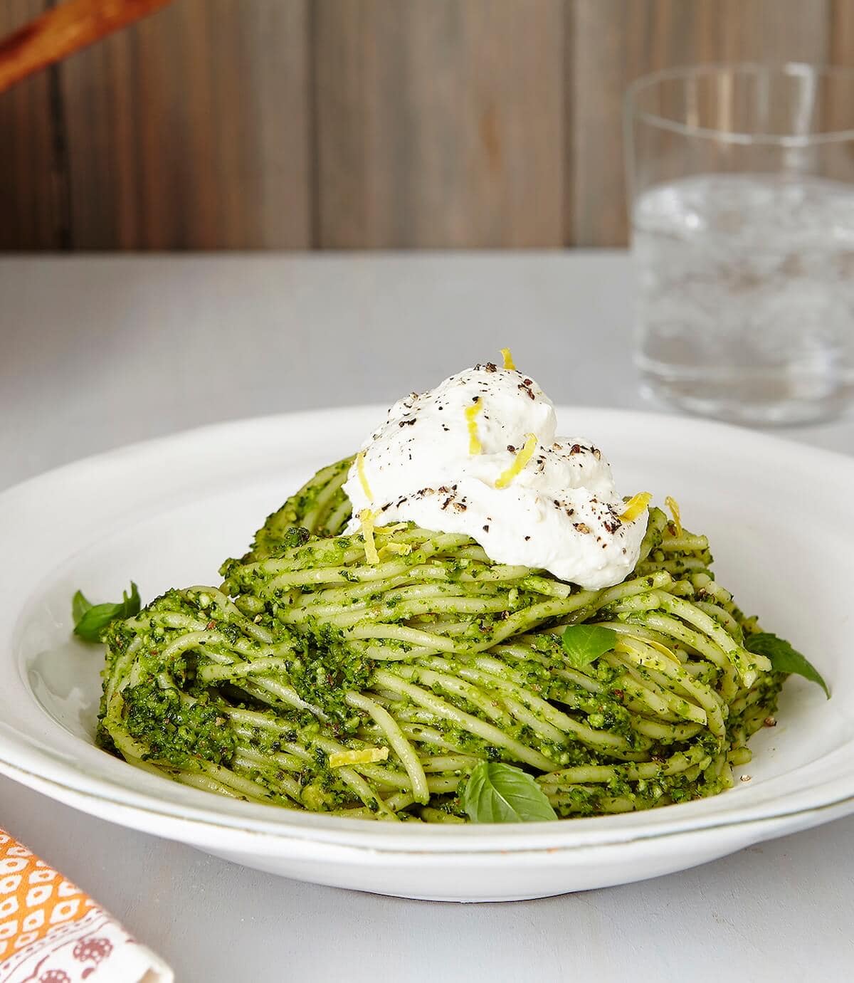 pesto pasta with lemon ricotta in a white bowl with glass of water.