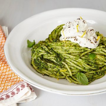pesto pasta with lemon ricotta in white bowl on white background.