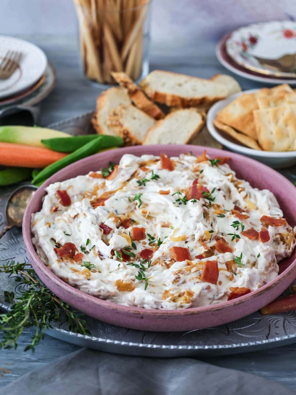 caramelized onion bacon dip with bread, crackers, and vegetables for dipping.