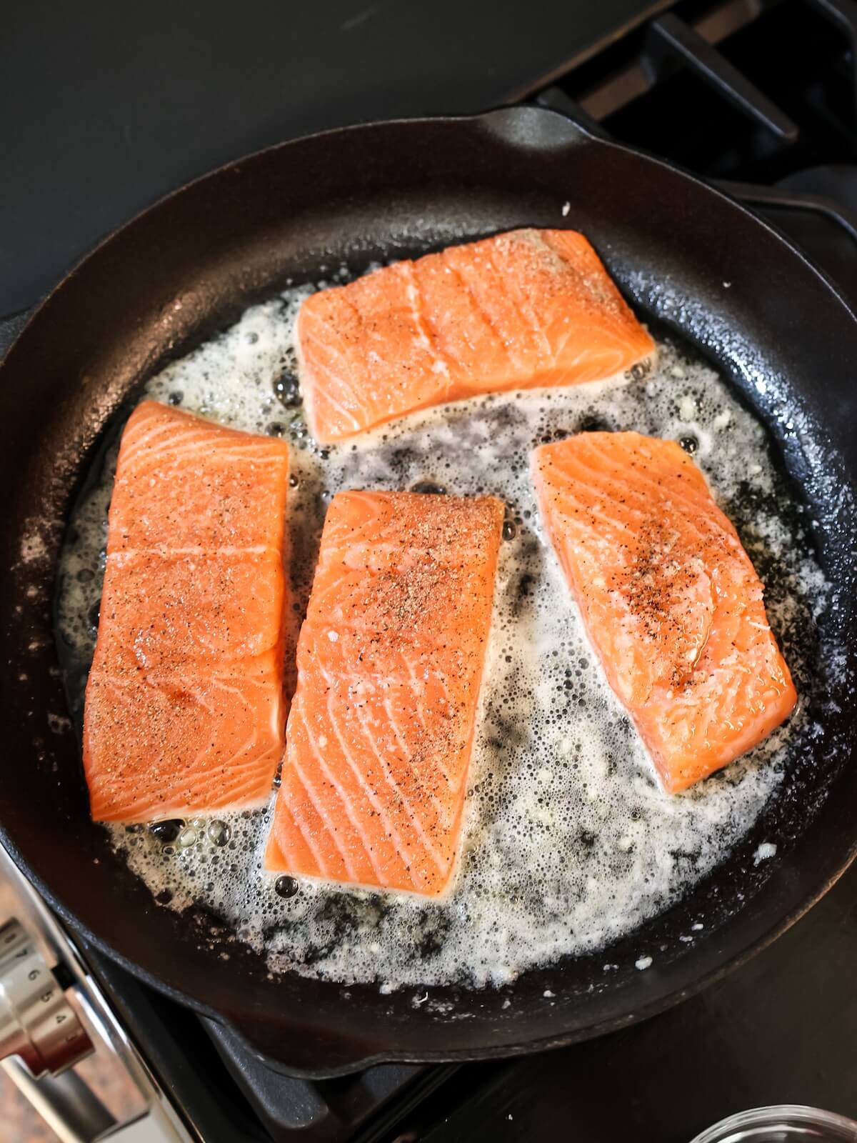 Cooking seasoned salmon in a cast iron skillet with butter.