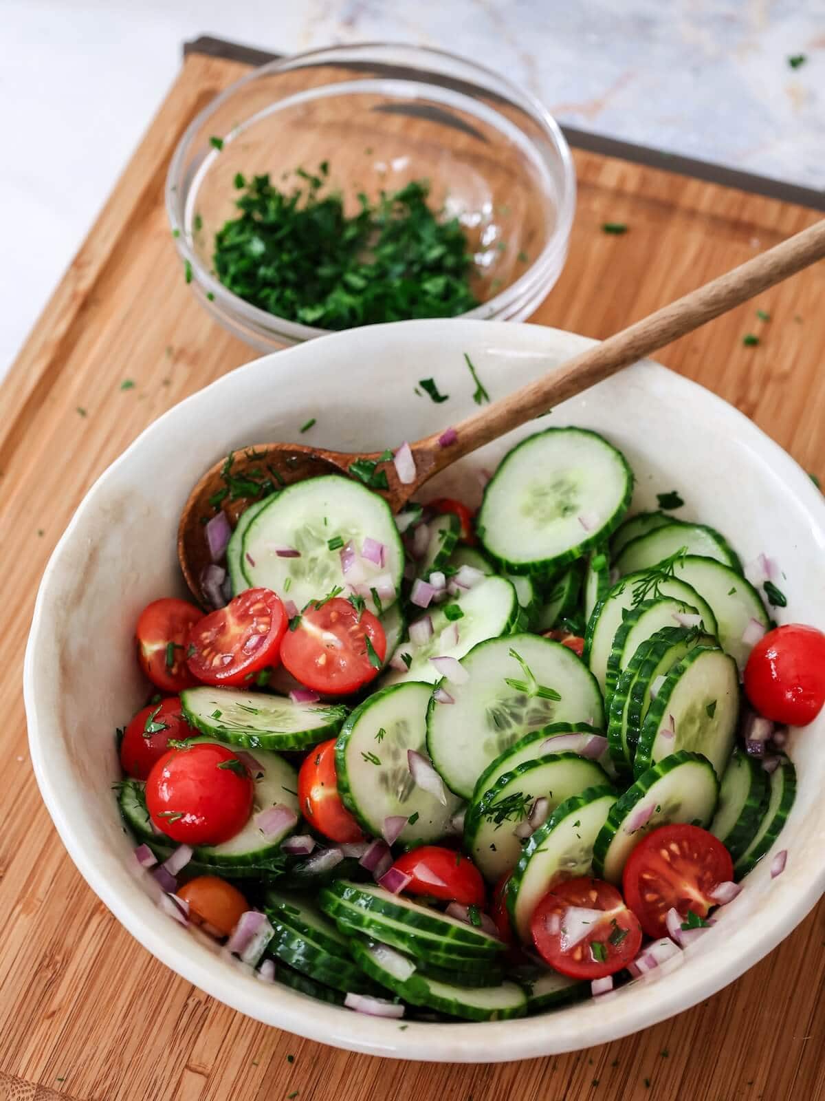 adding herbs and dressing to cucumber salad.