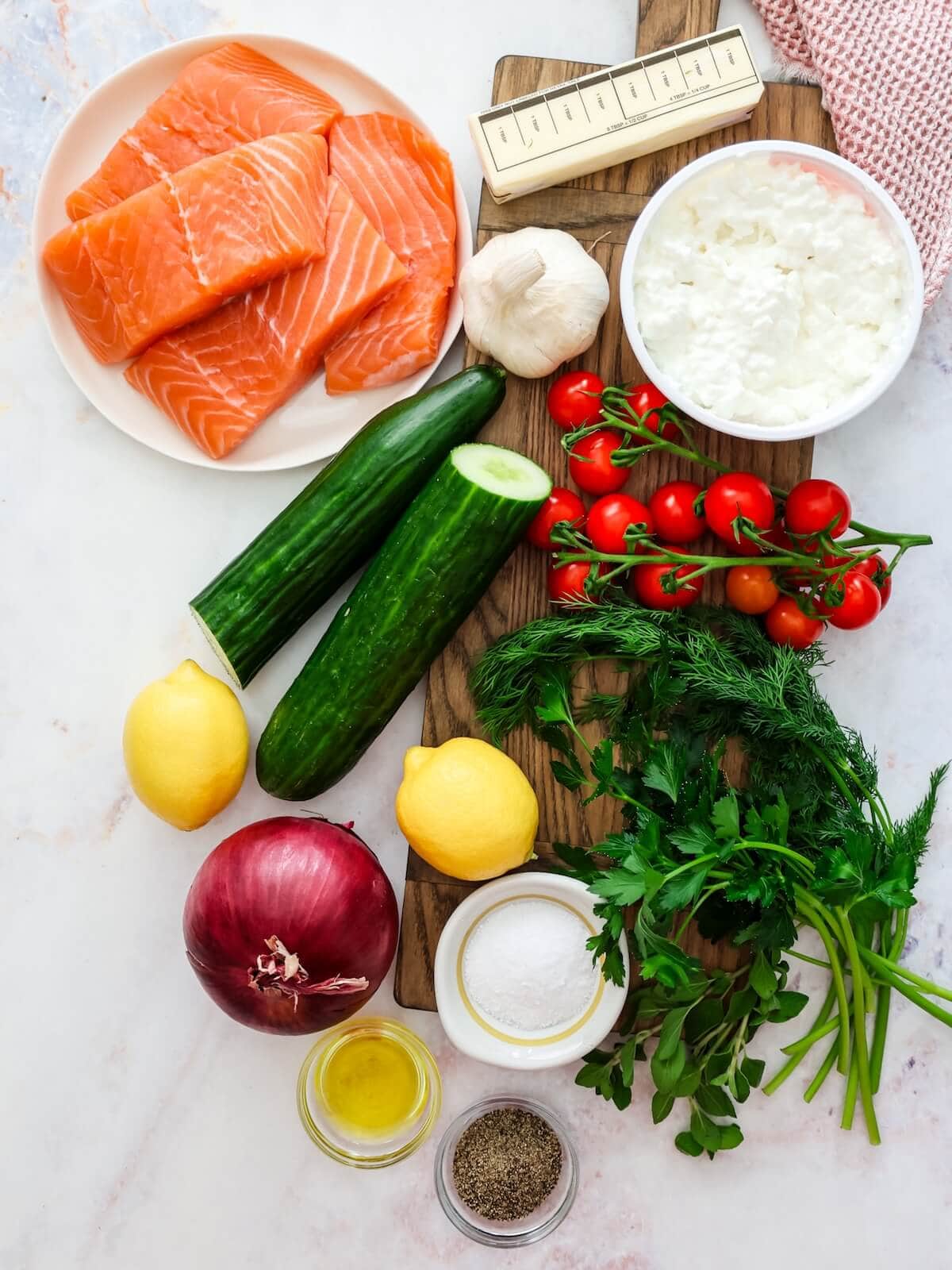 Ingredients for lemon butter salmon including cucumber salad, salmon, butter, garlic, lemon, and cottage cheese.