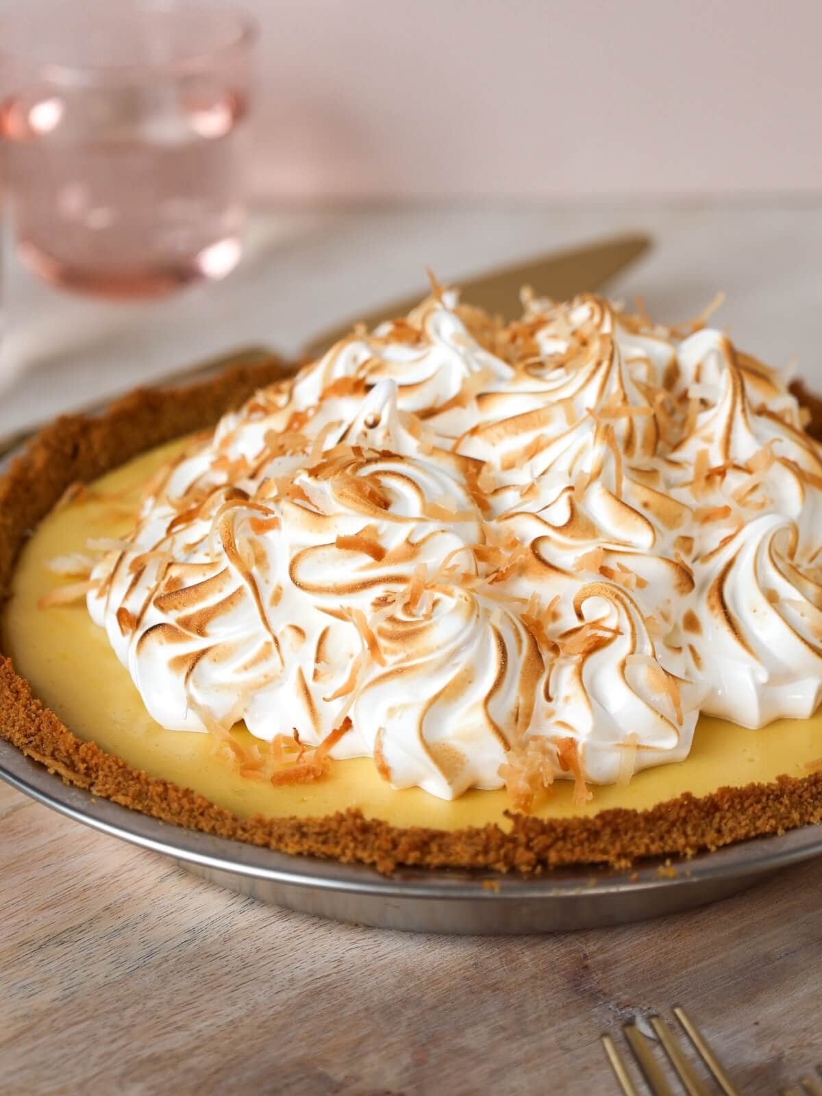 Side view of the whole mango meringue pie, showing piped meringue swirls with toasted peaks and a thick graham crust.