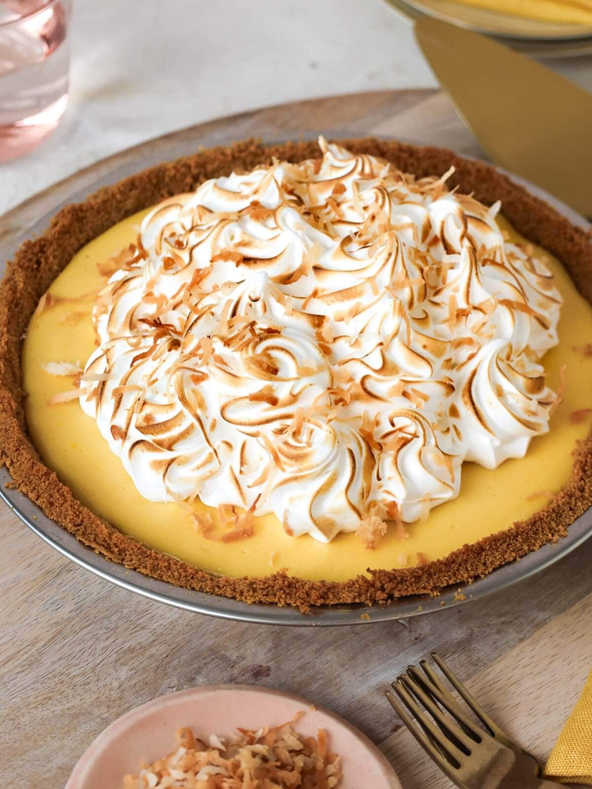 Whole mango pie with golden graham cracker crust and a mound of piped meringue, topped with toasted coconut.