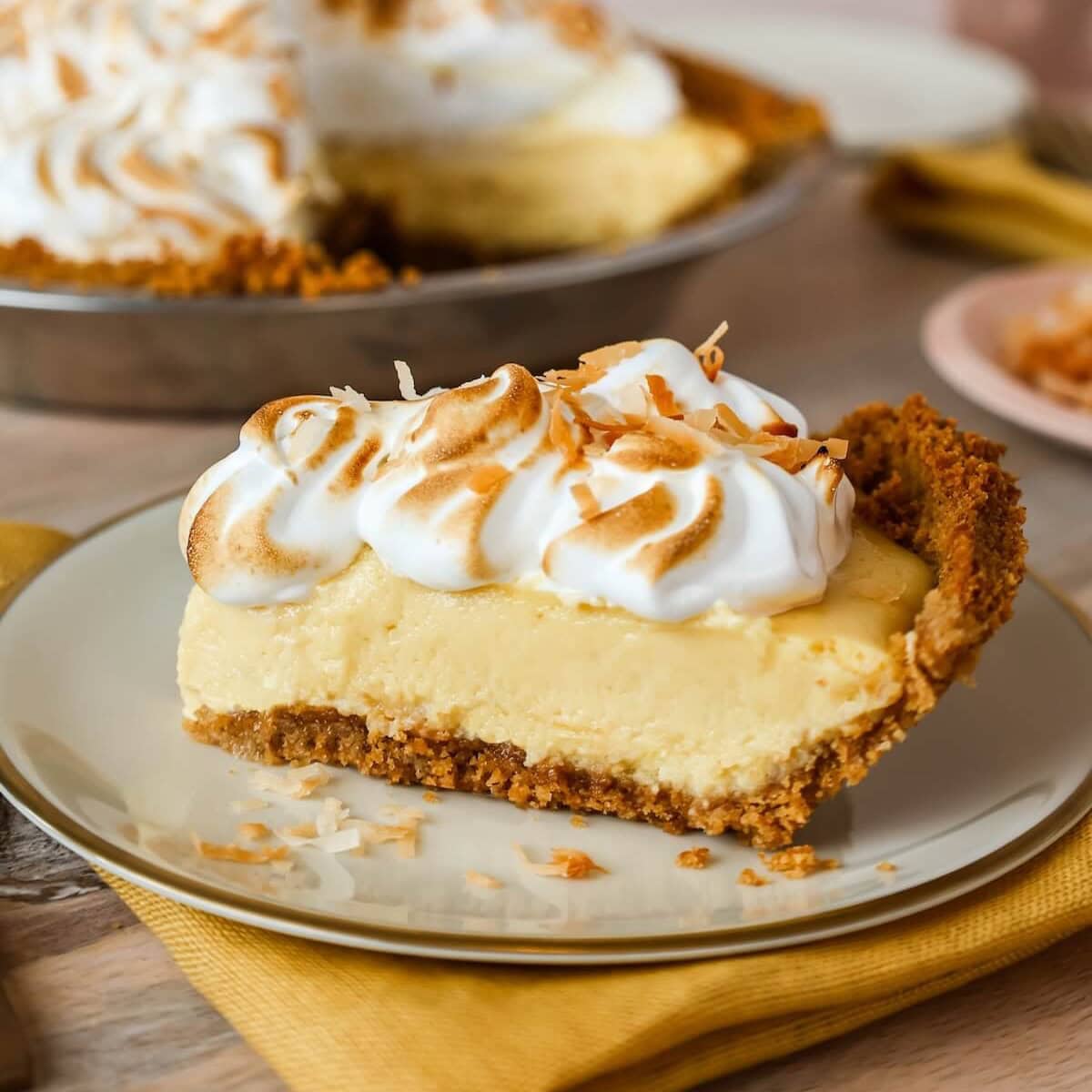 Slice of mango pie with graham cracker crust and toasted meringue topping on a plate, garnished with shredded coconut.
