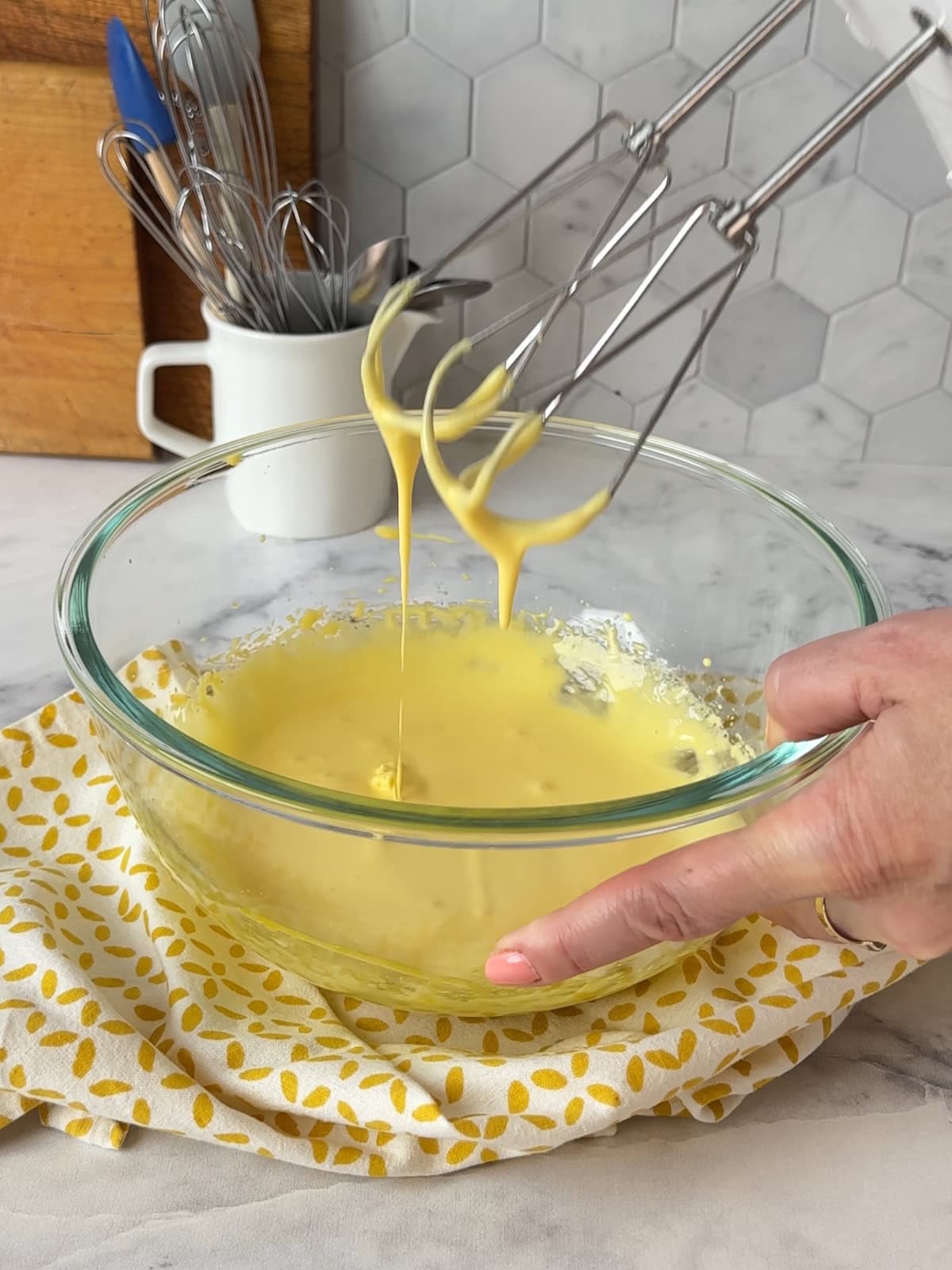 Lifting thickened eggs with beaters over a mixing bowl, showing smooth texture.
