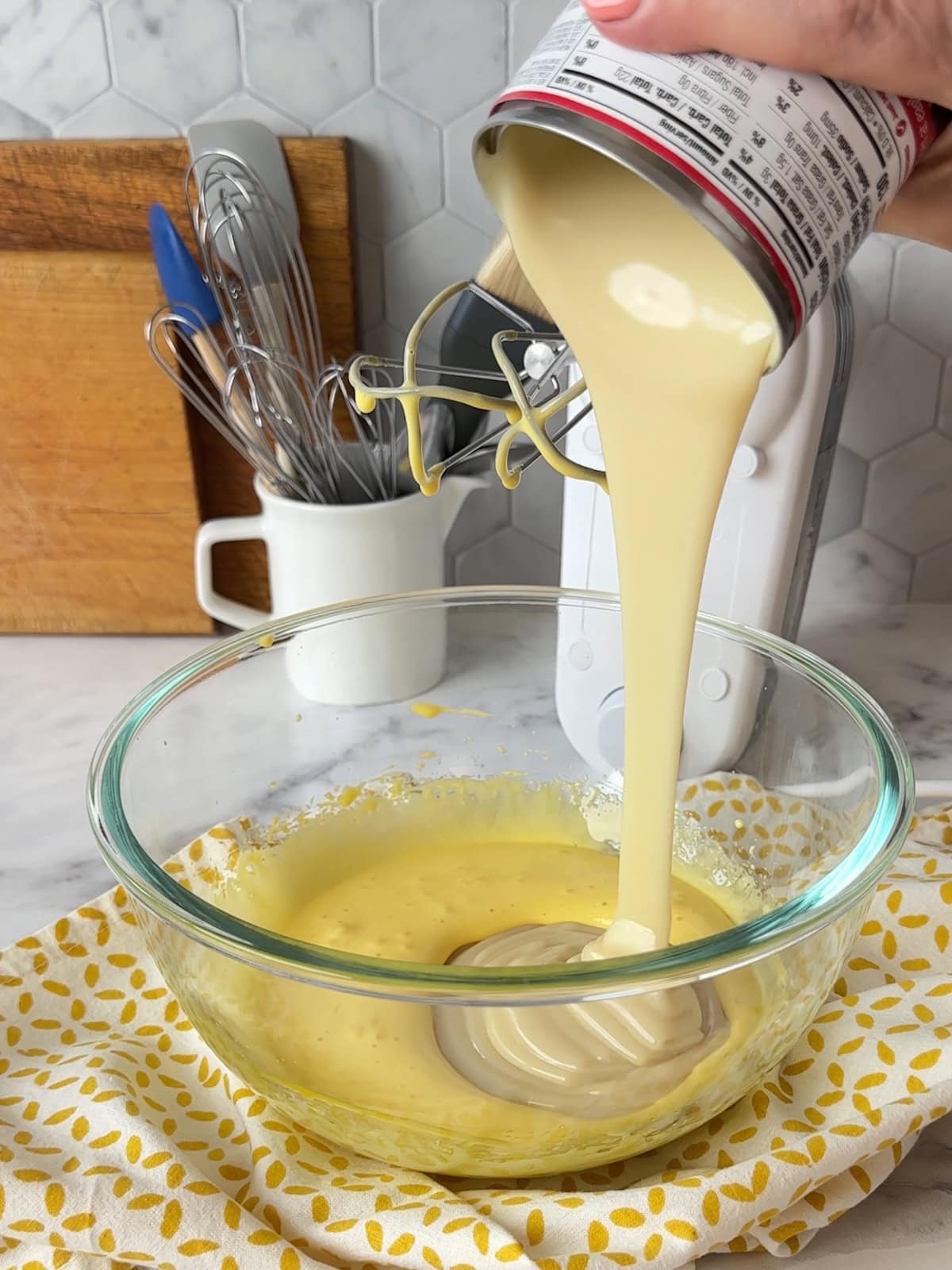 Pouring sweetened condensed milk into a bowl of beaten egg yolks to make the filling.