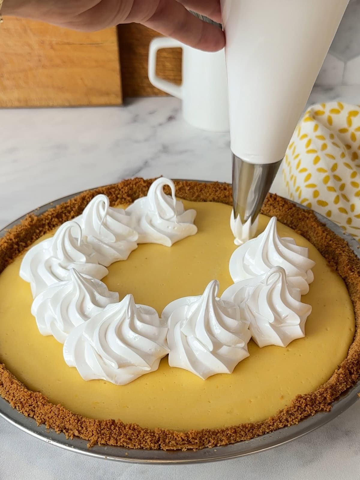 Piping tall swirls of meringue onto the chilled mango pie using a pastry bag with a star tip.