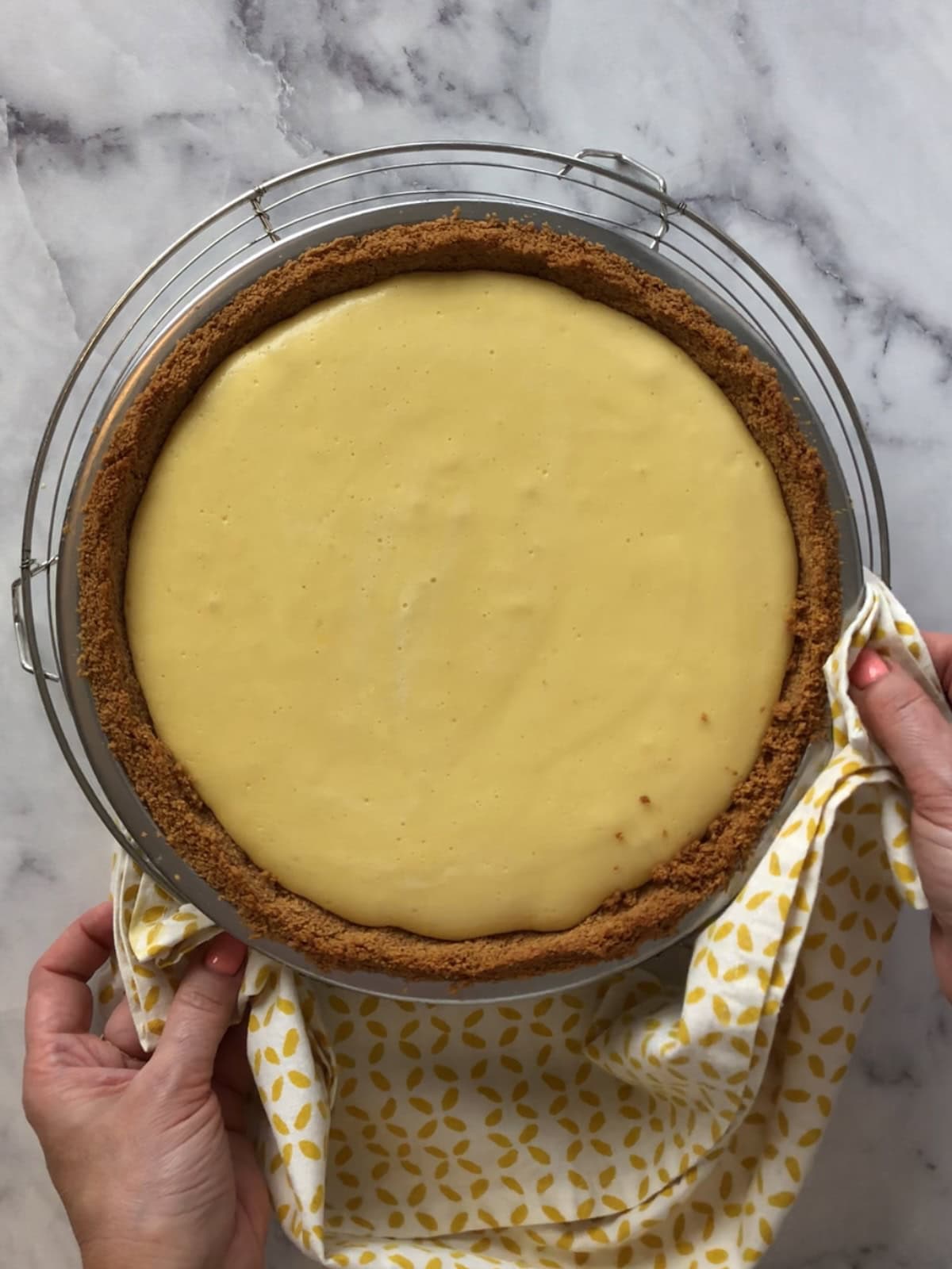 Holding a baked mango pie with smooth filling and golden crust, resting on a cooling rack.