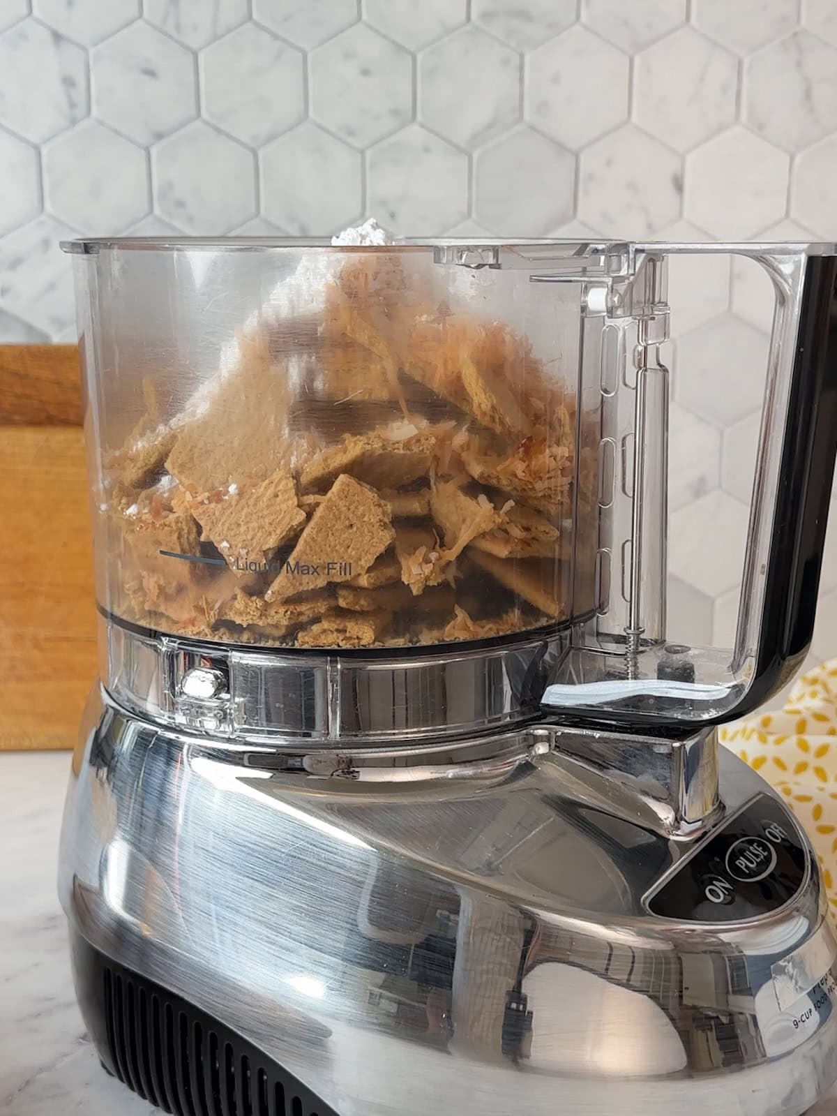 Graham crackers and shredded coconut in a food processor bowl, ready to be pulsed into crust crumbs.