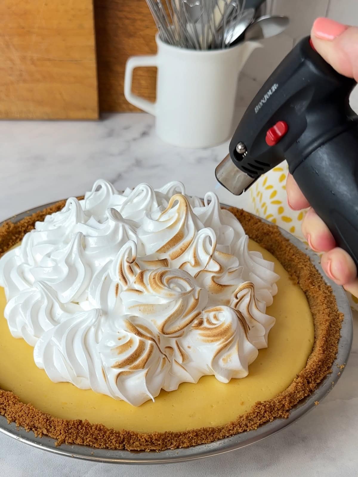 Torching the meringue topping with a kitchen torch to create golden toasted peaks.