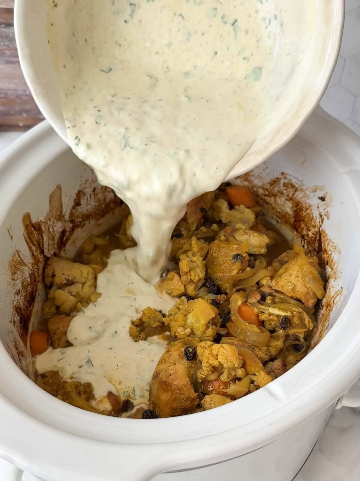 Pouring the creamy yogurt and herb sauce back into the slow cooker over the chicken and vegetables.