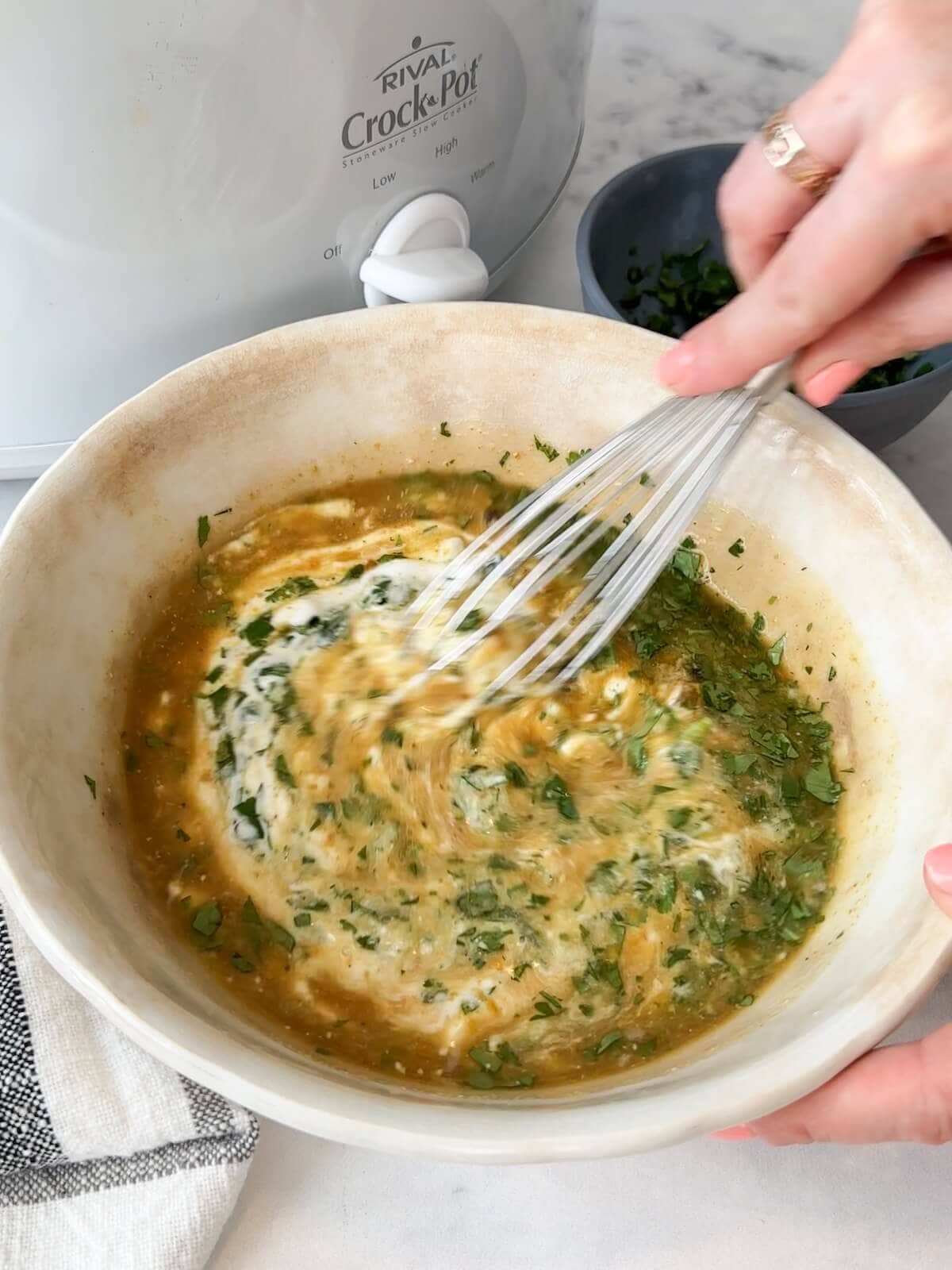 Whisking hot curry broth with yogurt and chopped herbs in a mixing bowl.
