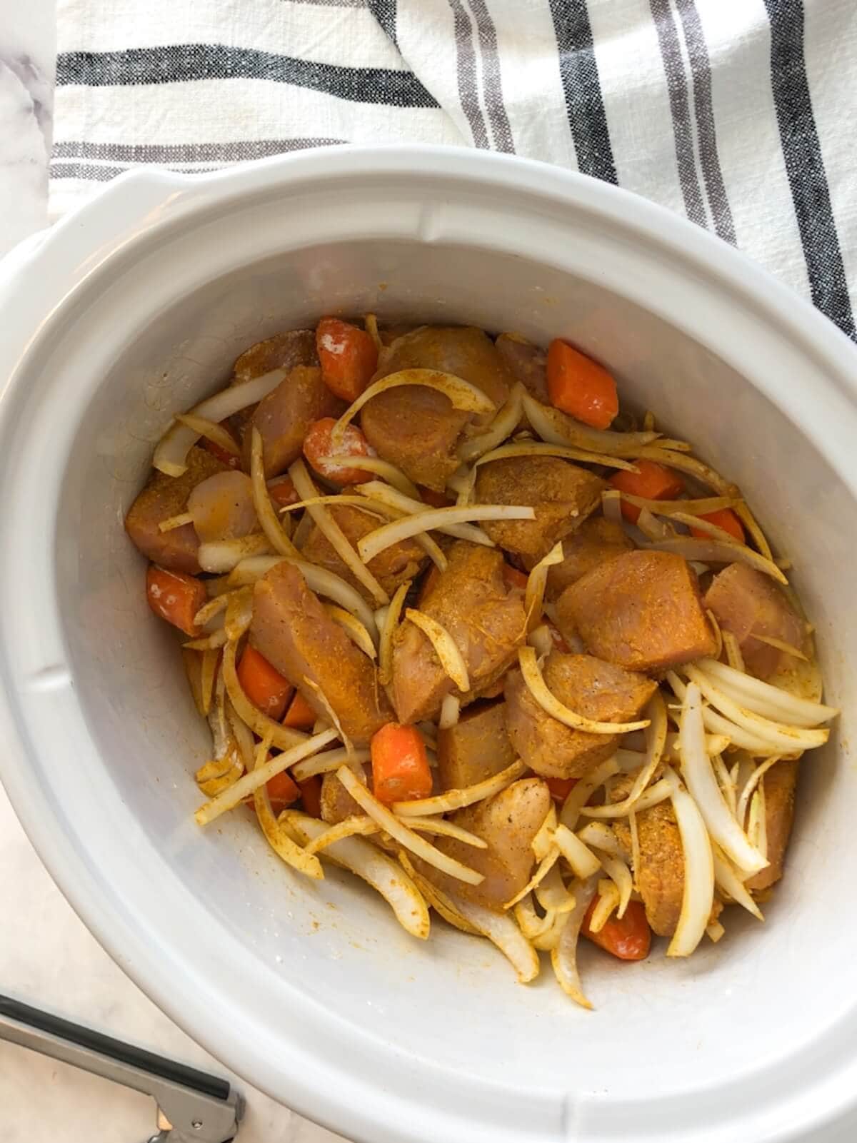 Chicken, onions, and carrots mixed with spices inside the slow cooker, ready to cook.