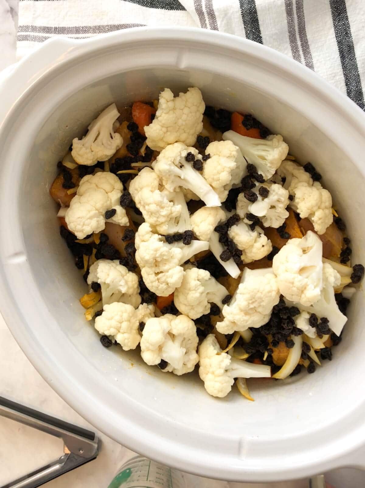 Cauliflower florets and currants added on top of the chicken mixture in the slow cooker.