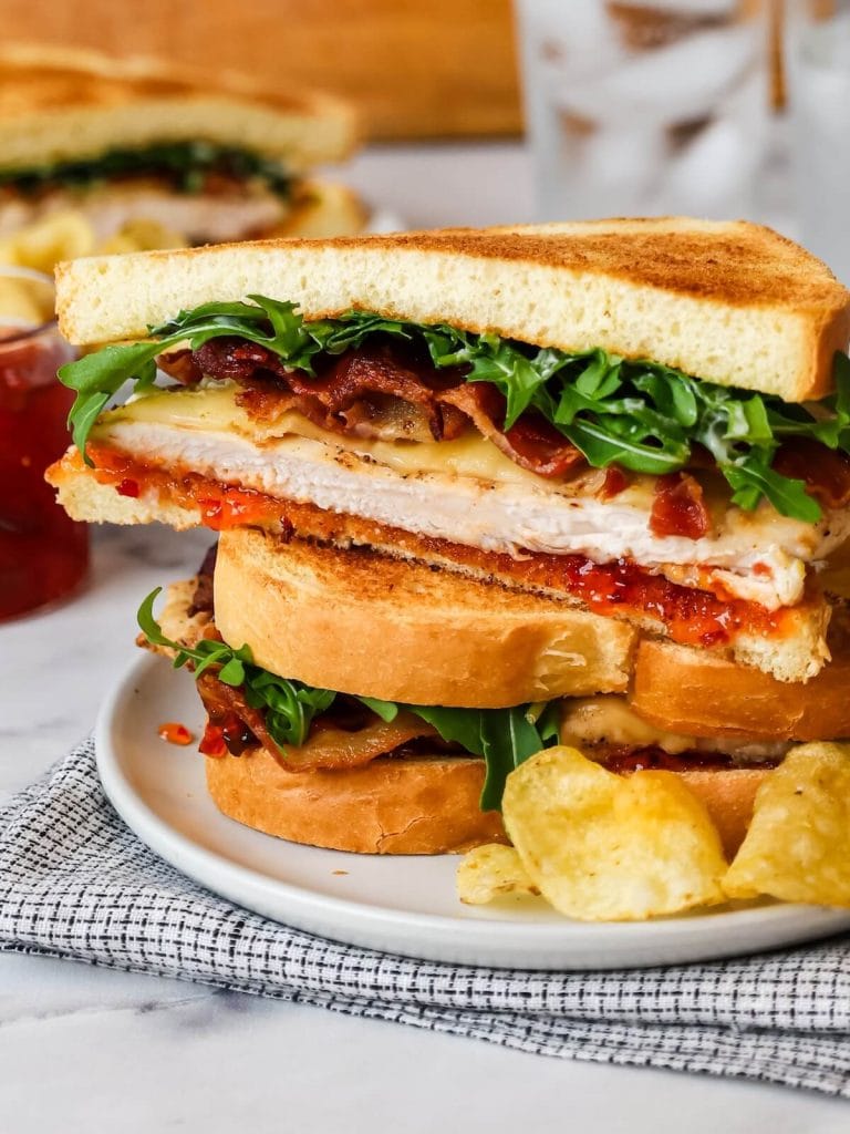 chicken bacon sandwich cut open on a plate with potato chips.