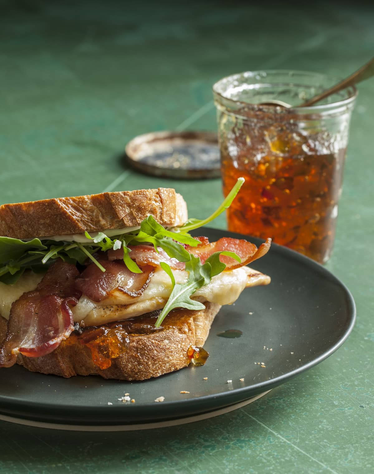 Beauty shot of chicken bacon sandwich on a dark plate with pepper jelly.