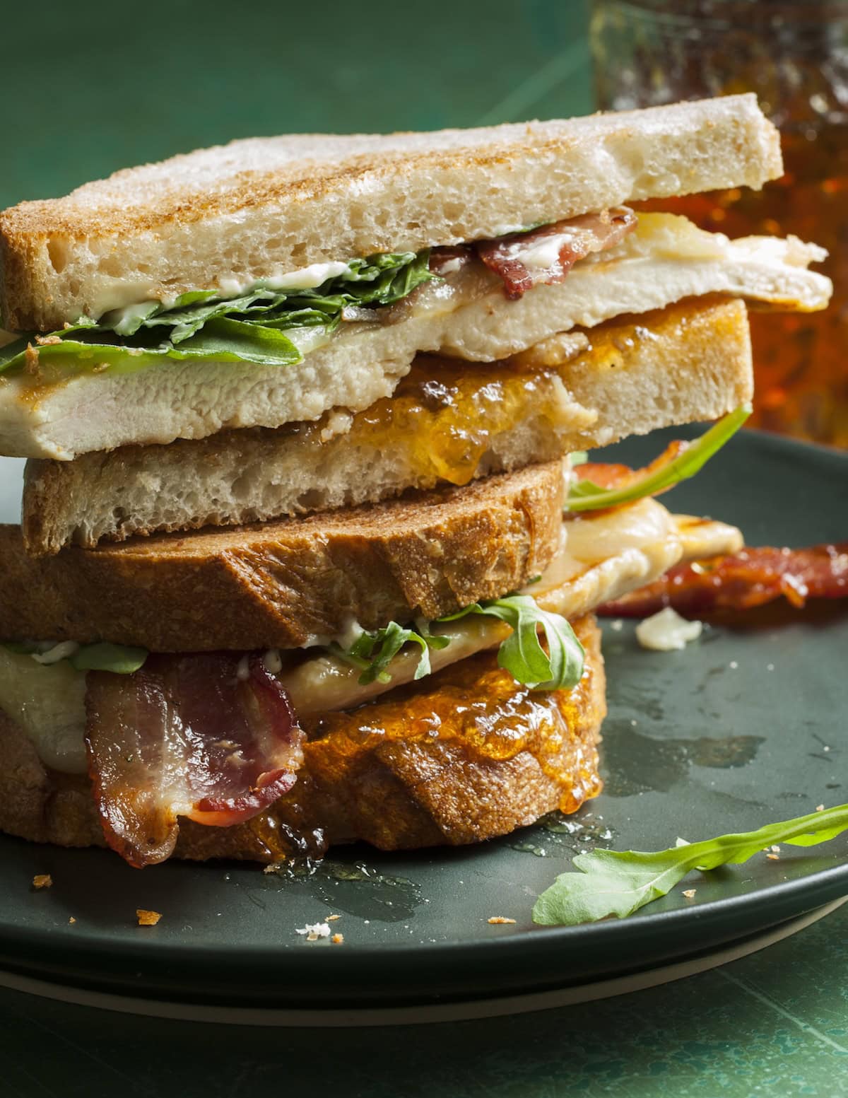 A sandwich on a plate with bacon and chicken and pepper jelly.