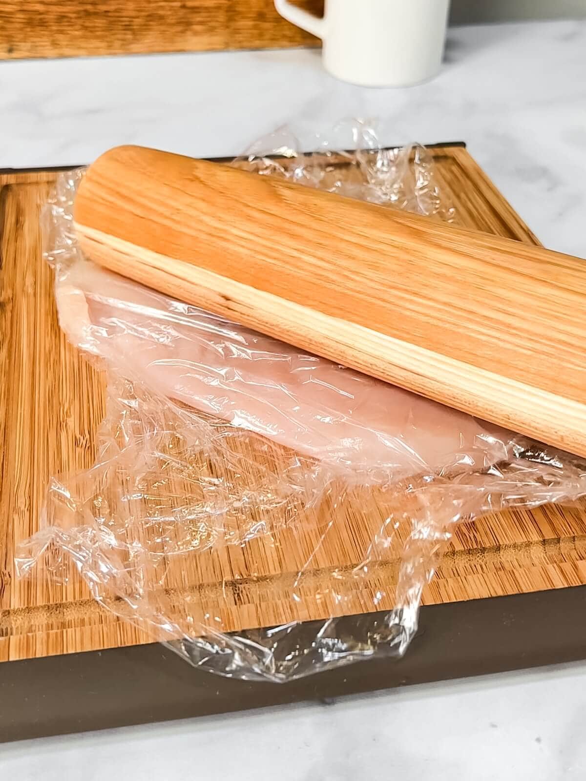 pounding a chicken breast flat with a rolling pin.