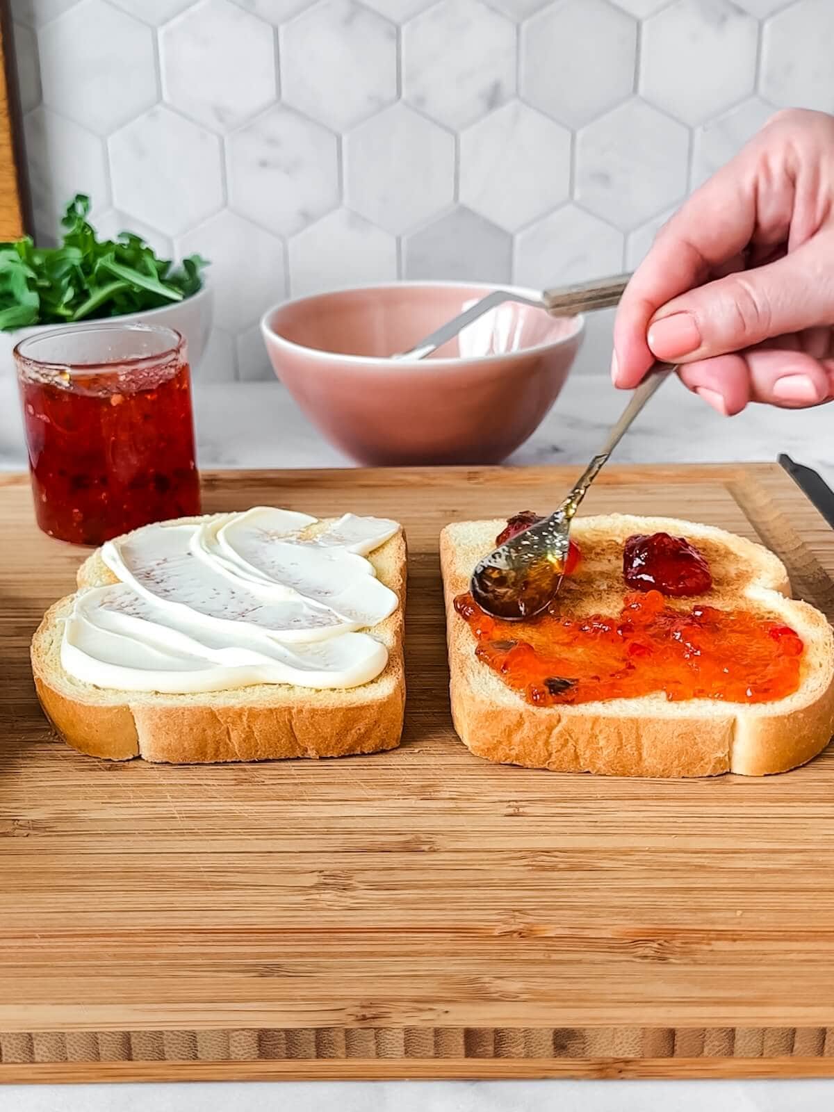 sweet and spicy chicken bacon sandwich being assembled on a cutting board with mayo and sweet pepper jelly.