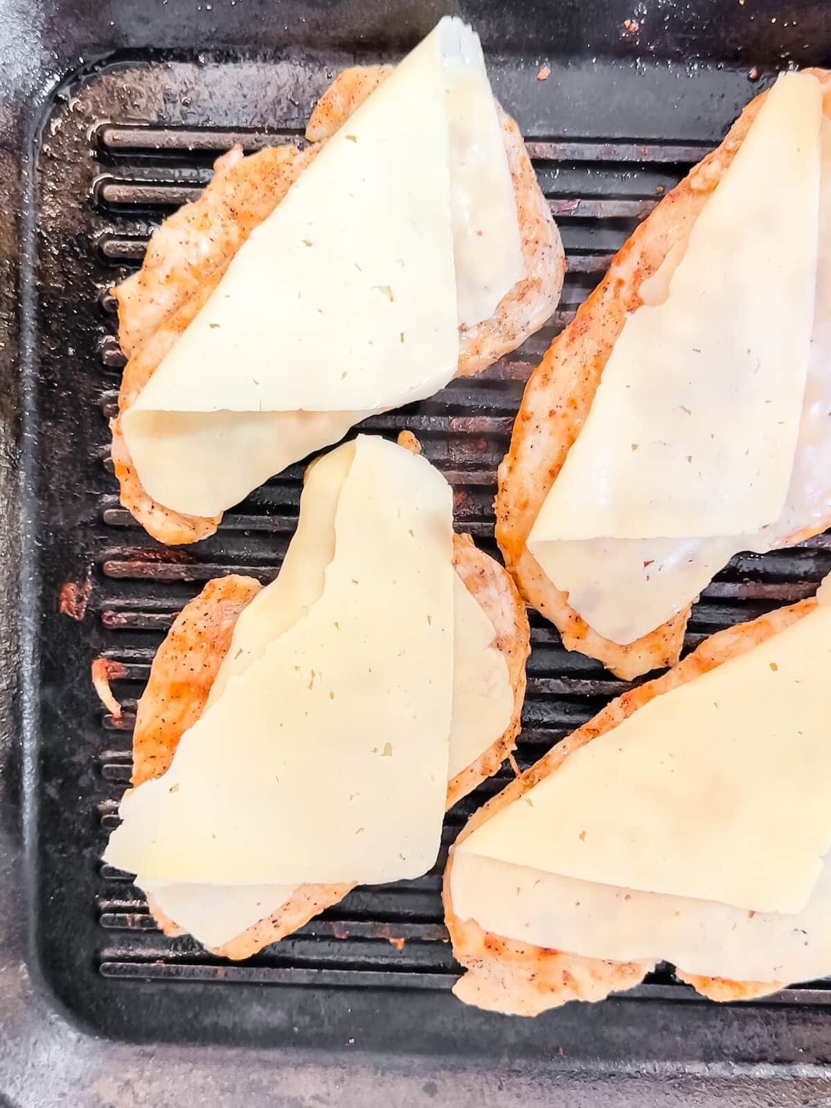 Four pieces of chicken on a grill with cheese on top.
