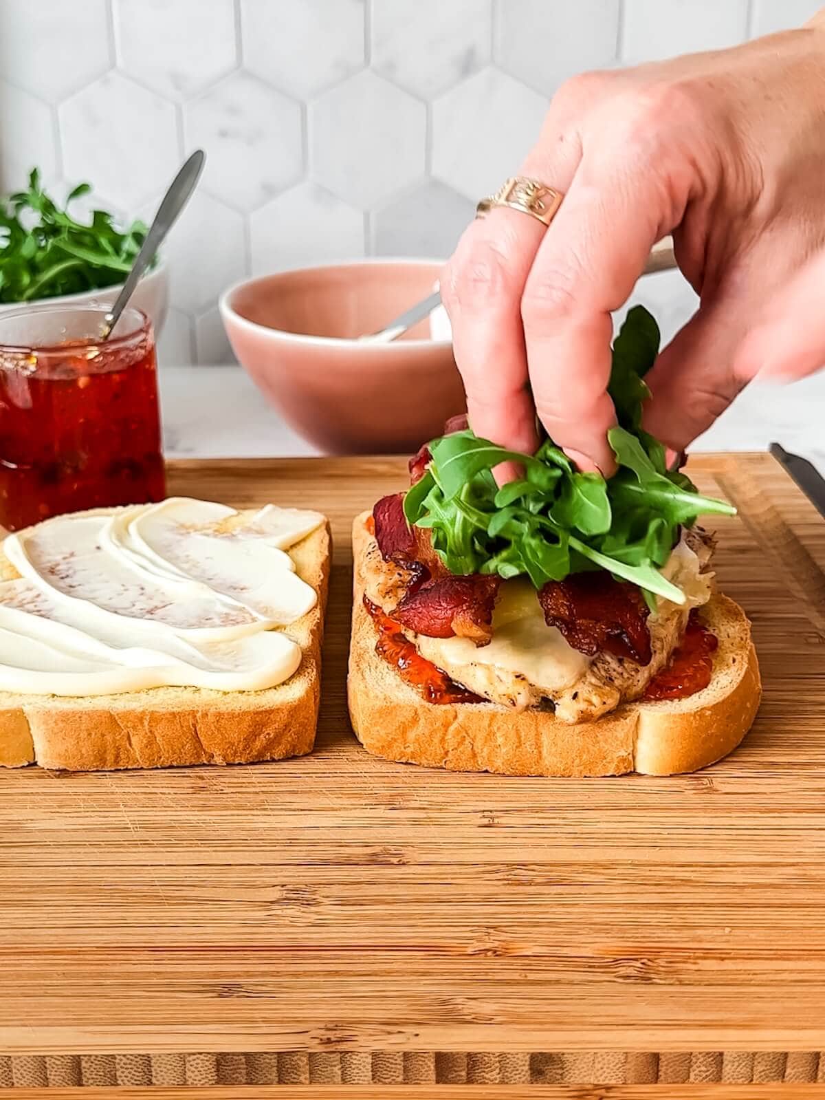 A person putting arugula on a sandwich on a cutting board