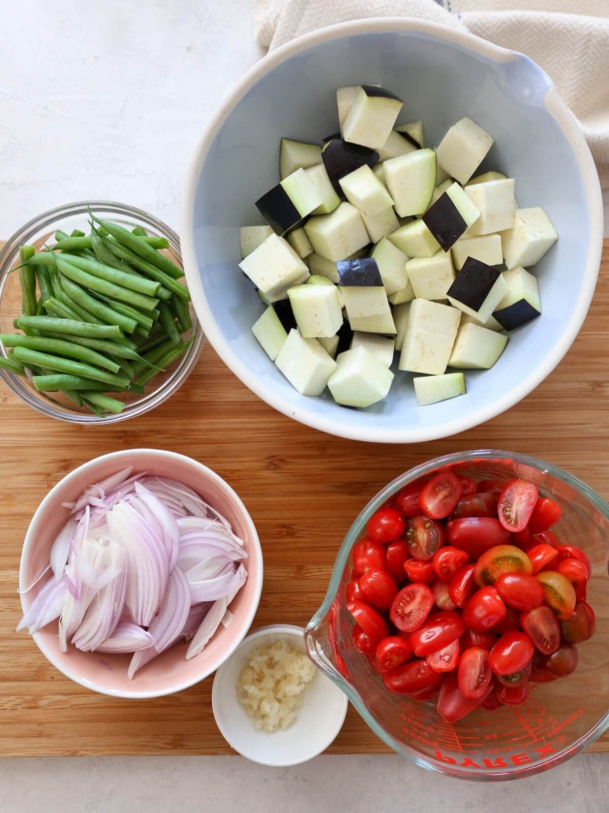 Prepped and cut veggies for eggplant pasta including eggplant, beans, shallots, tomatoes and garlic.