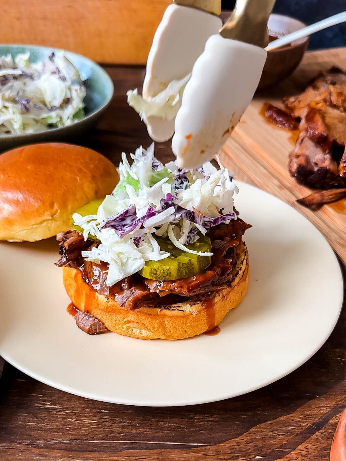 assembling slow cooker brisket sandwiches with pickles and coleslaw.