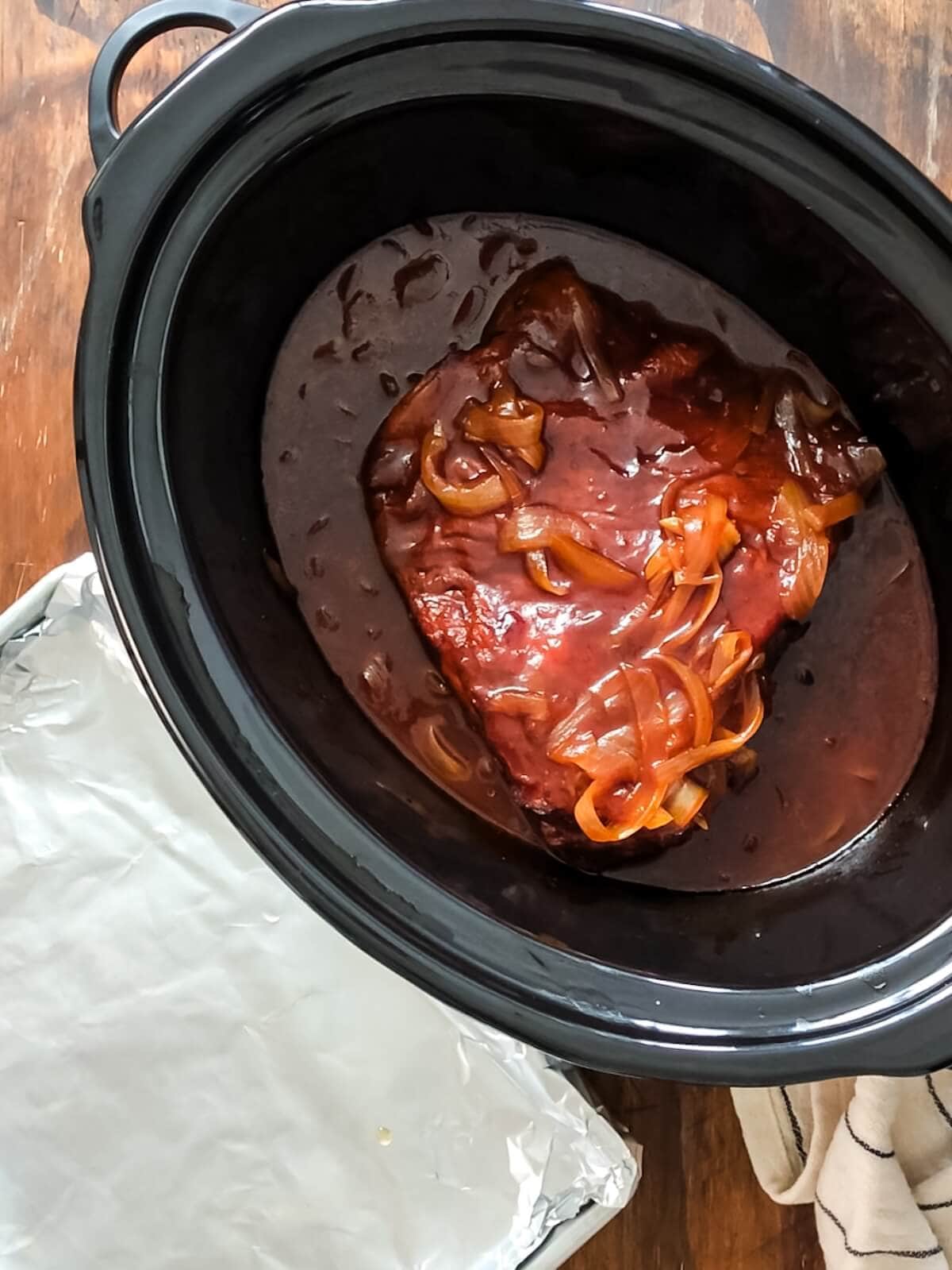 cooked brisket and onions in a slow cooker with BBQ sauce.
