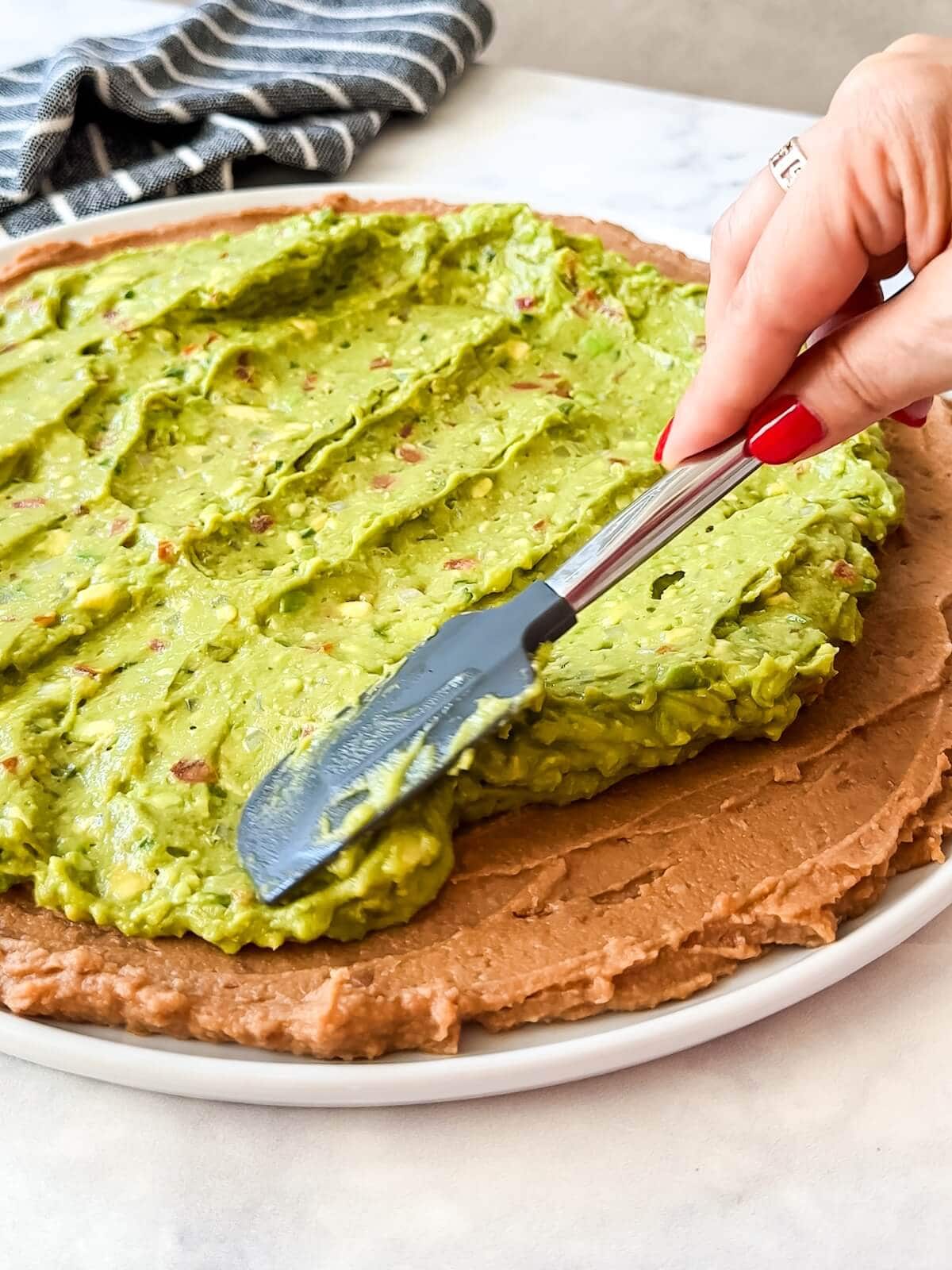 Adding a thin layer of guacamole to the top of bean dip for 7 layer dip