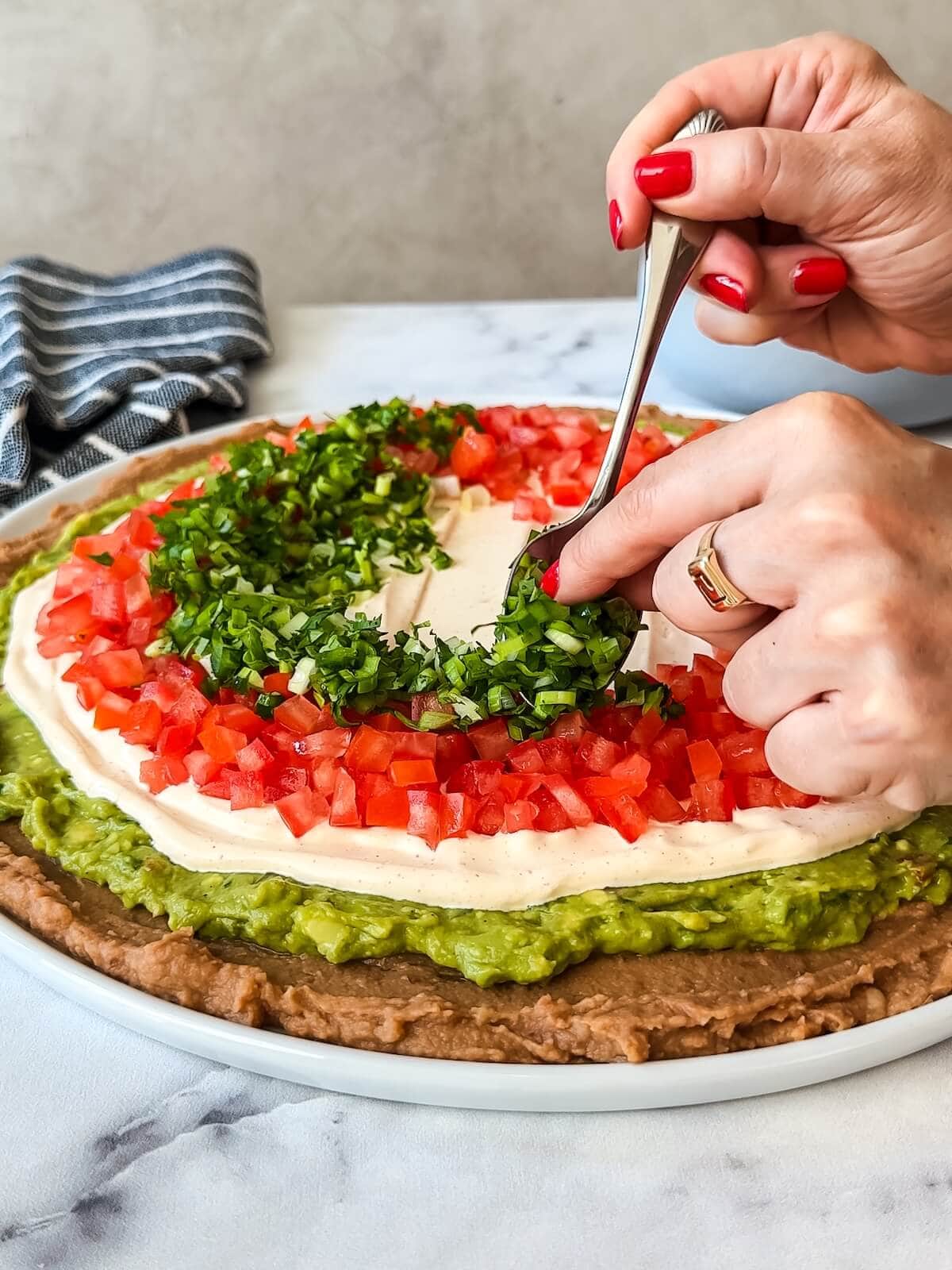 Adding green herb mixture to 7 layer dip in a ring