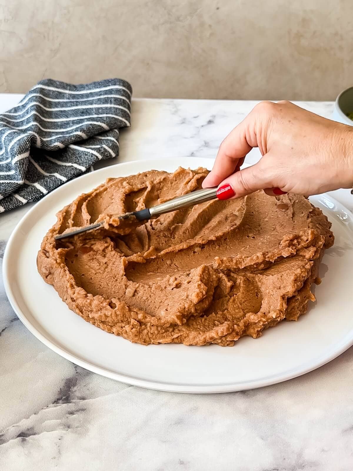 Spreading bean dip on a round white platter for the base of 7 layer dip.