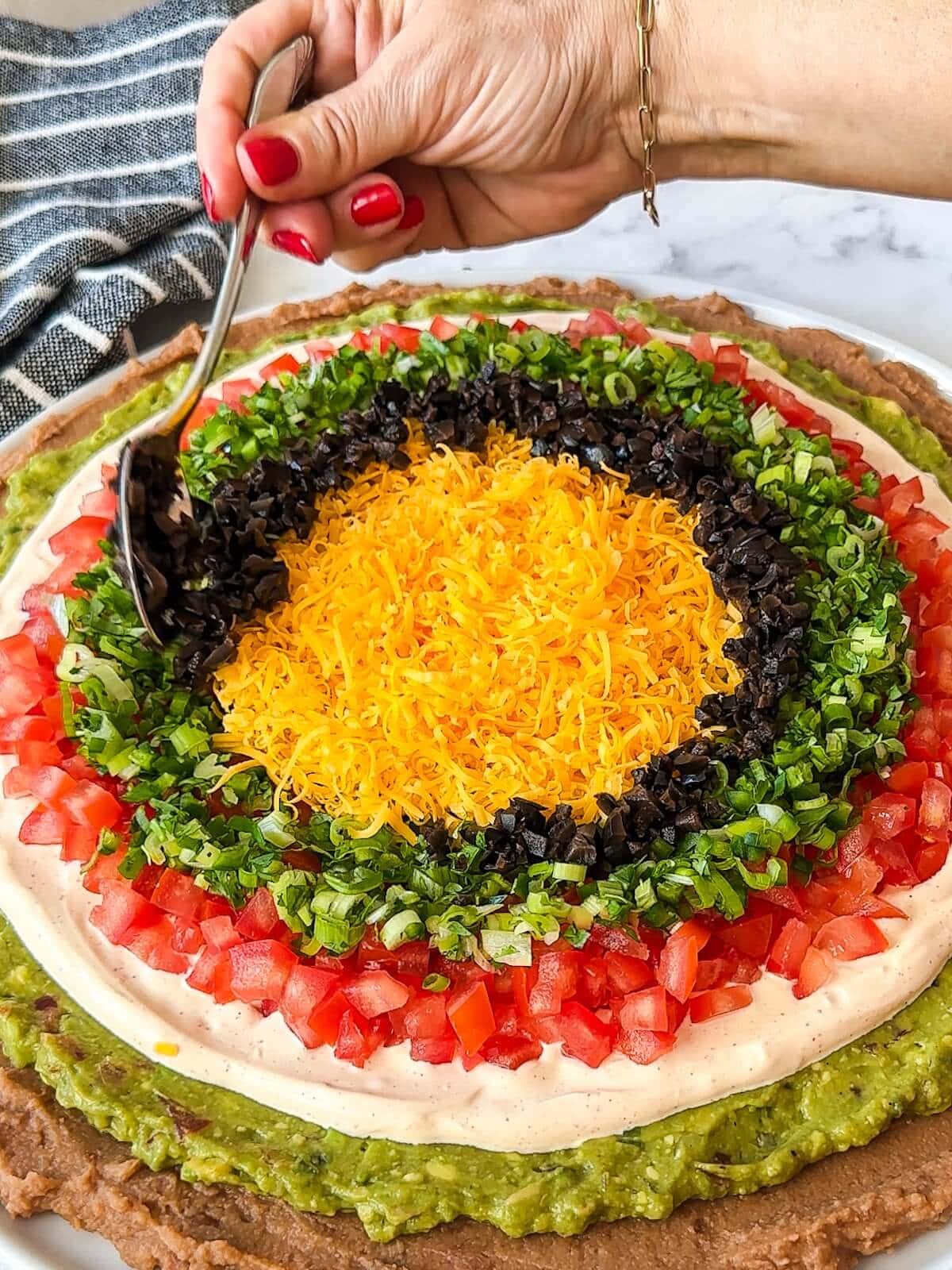 Adding the final ring of chopped olives to the dip