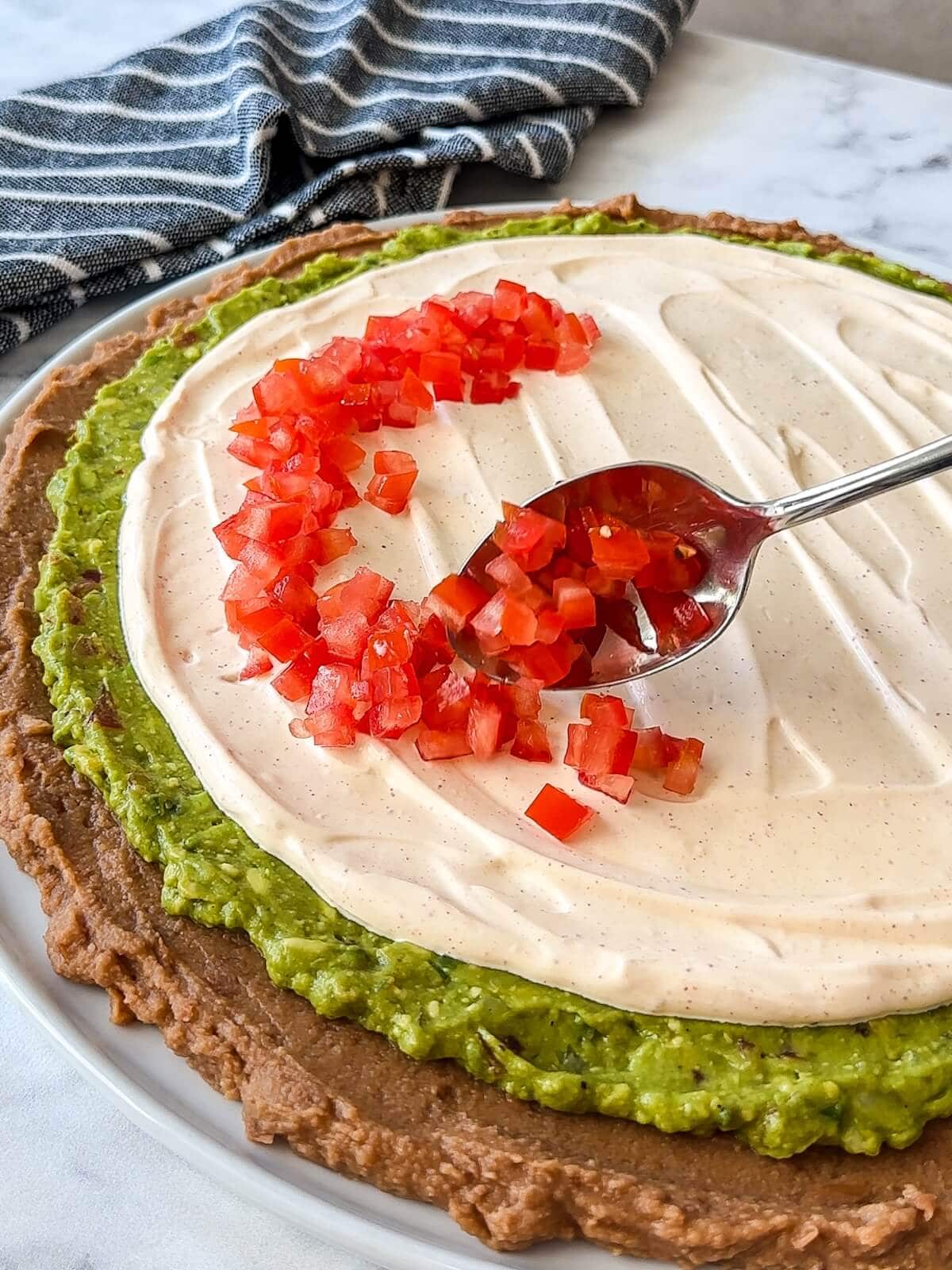 Carefully layering a ring of chopped tomatoes on the circle 7 layer dip