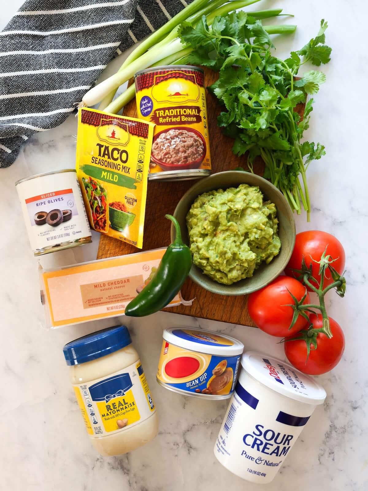 Ingredients for 7 layer dip on a white marble background.
