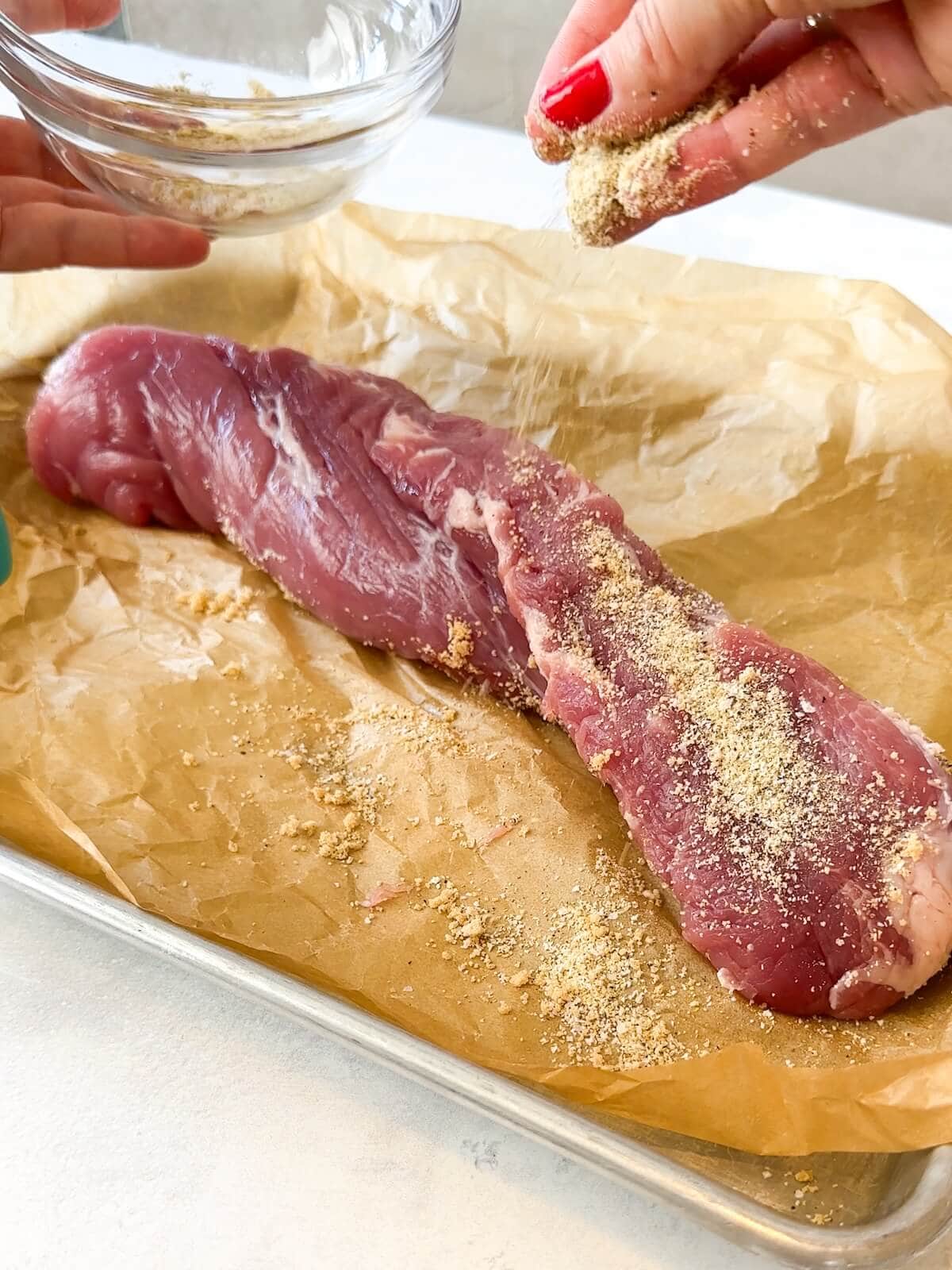 covering pork tenderloin with spice rub on parchment paper.