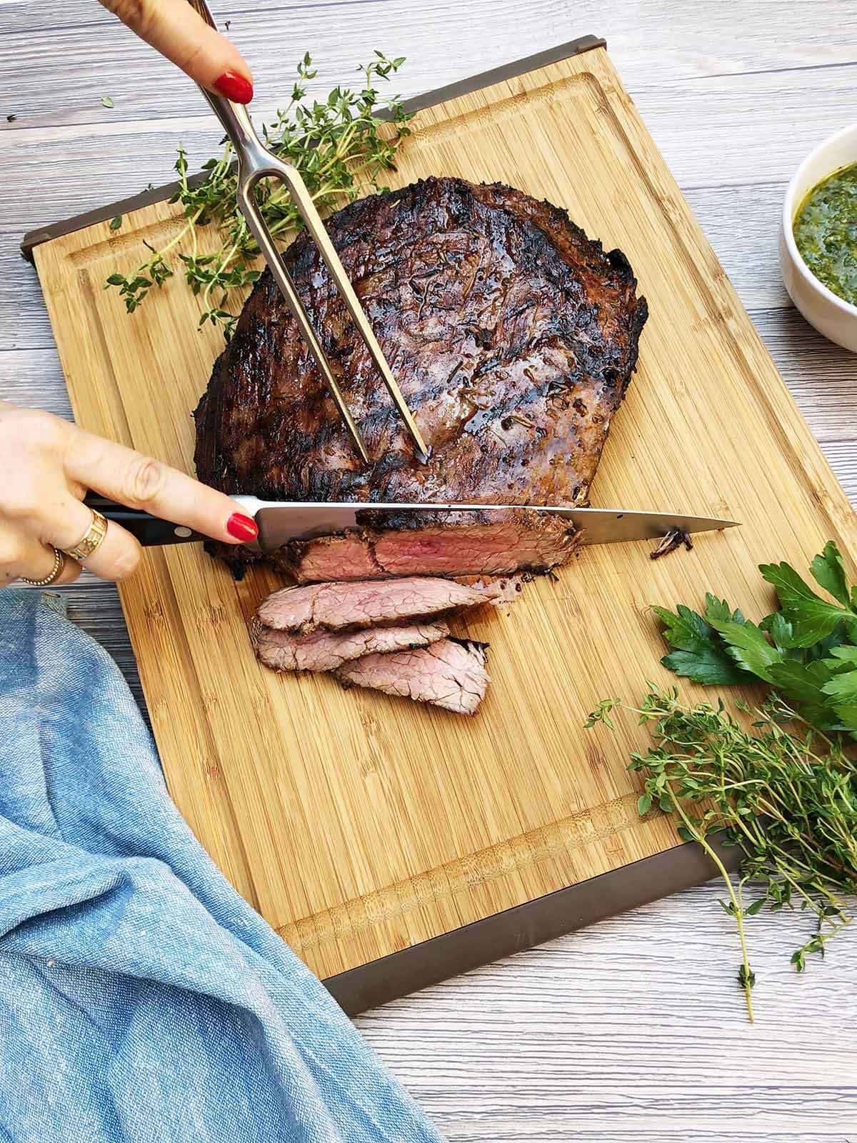 slicing grilled flank steak on a cutting board.
