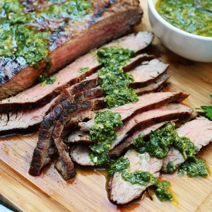 slices of grilled flank steak on a cutting board with fresh salsa verde