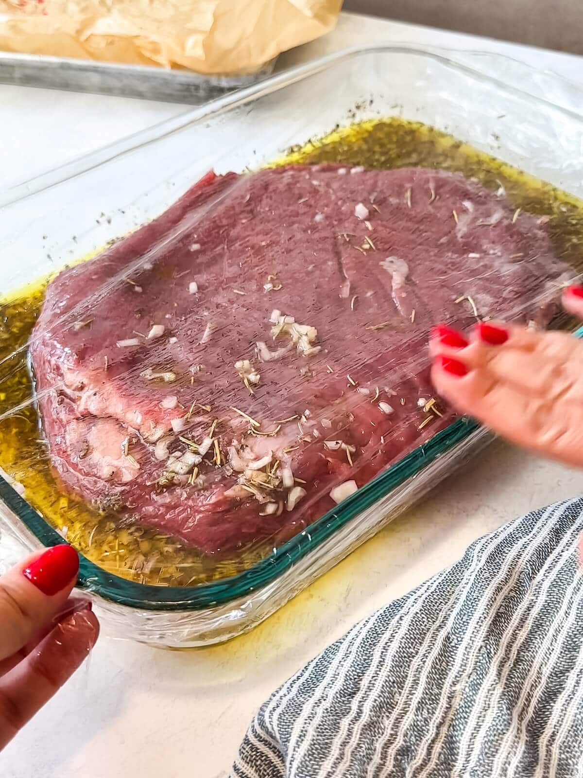 covering dish of marinating flank steak to store in the fridge.